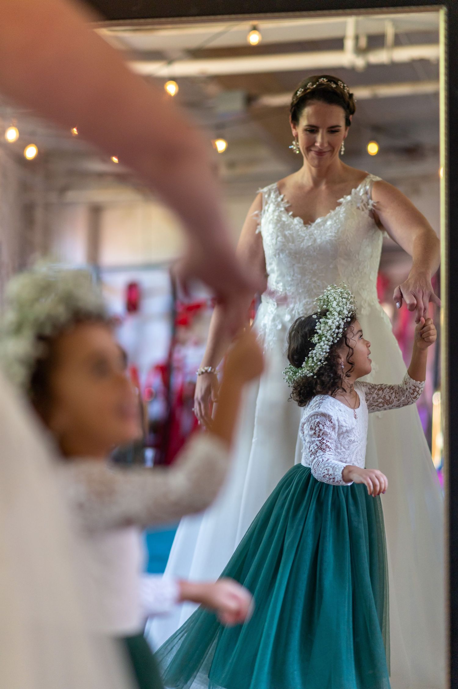 A bride in a white lace dress dancing with a young flower girl in an emerald green skirt.