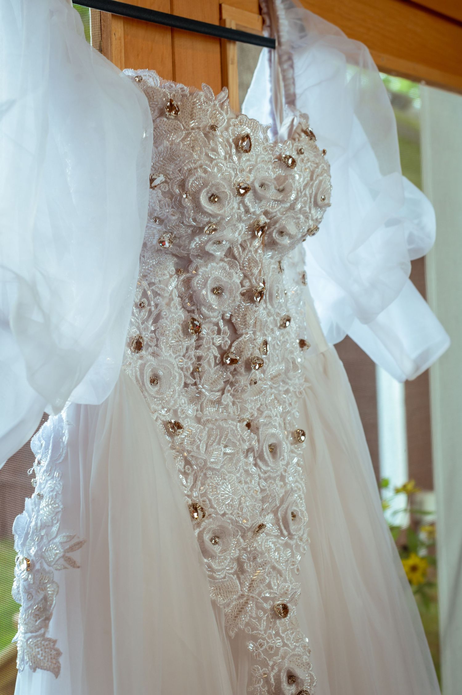 An elegant white wedding dress with intricate lace details and floral embellishments hangs on display.
