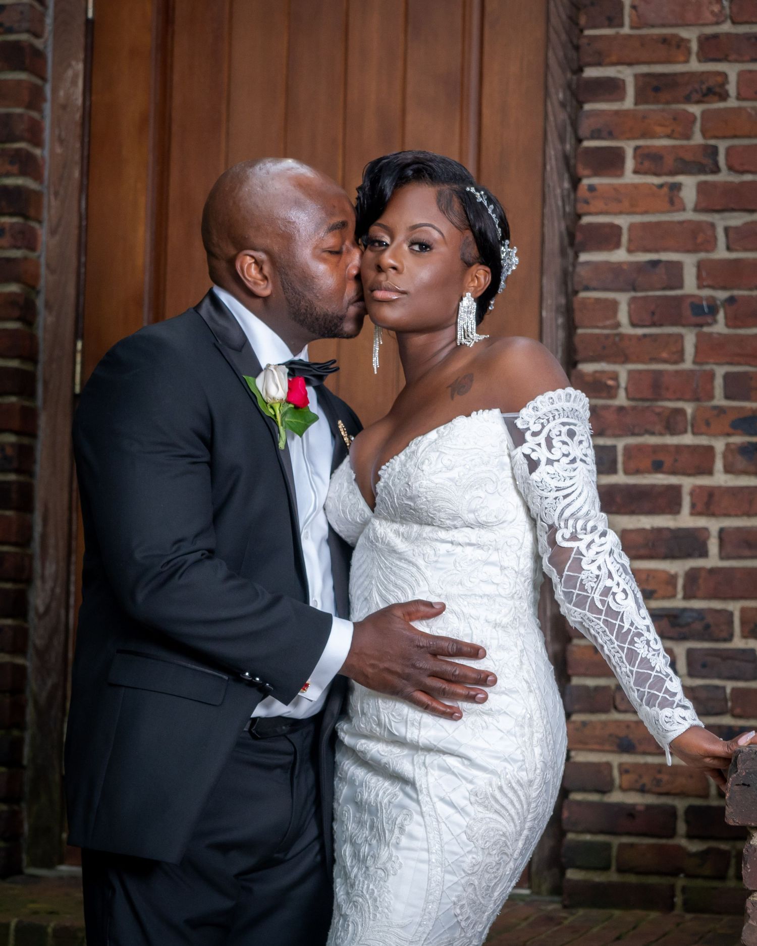 Romantic wedding portrait of couple in formal attire against brick wall.