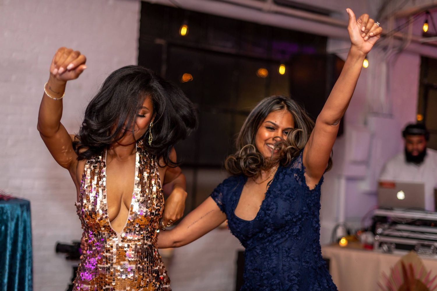 Two people dancing joyfully at a celebration event with sparkling dresses and raised arms.