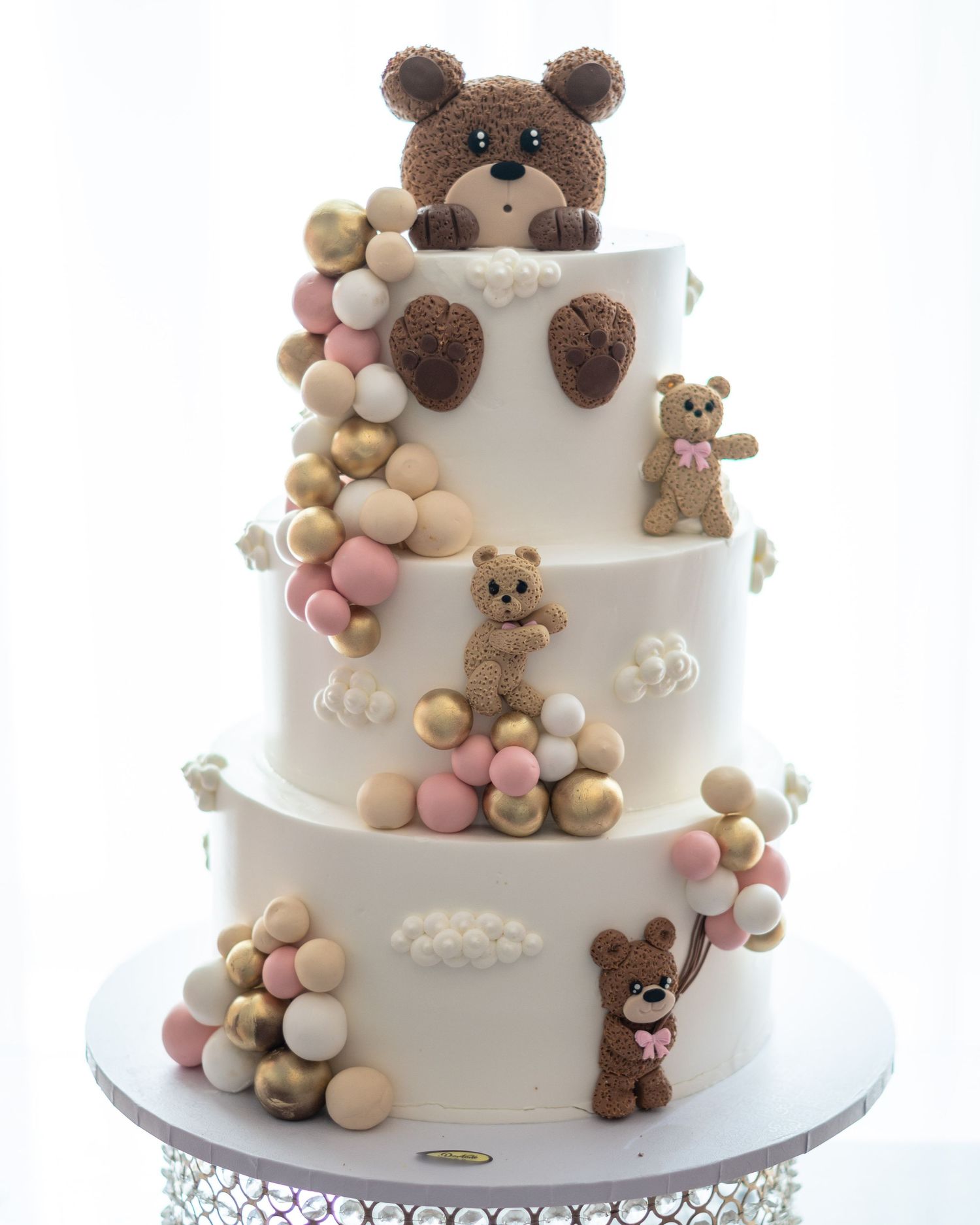 Three-tiered white cake decorated with adorable teddy bear figures and pastel ball decorations.