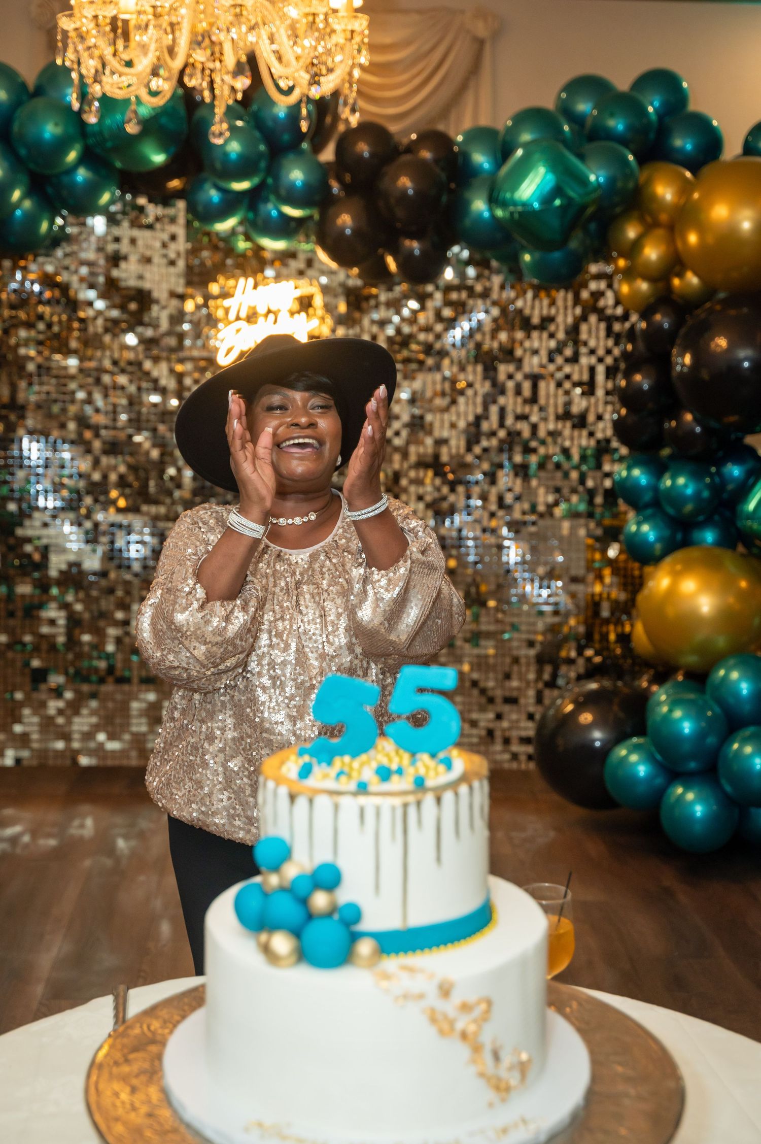 Celebratory scene with teal and gold balloons surrounding a two-tier 55th birthday cake.