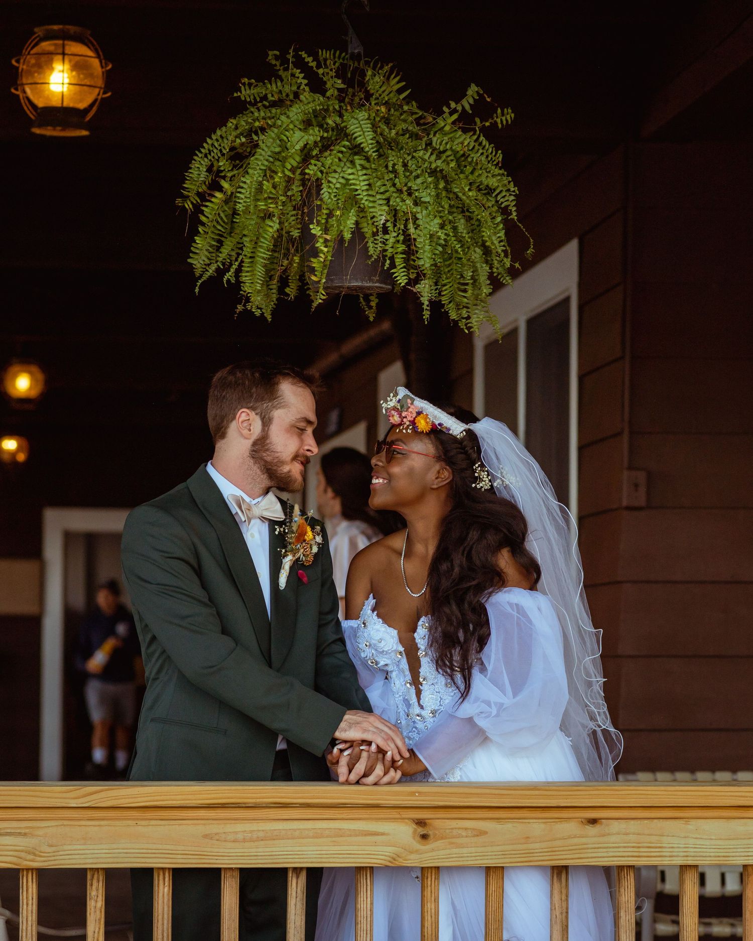 Romantic evening portrait of newlyweds on wooden deck with hanging fern.