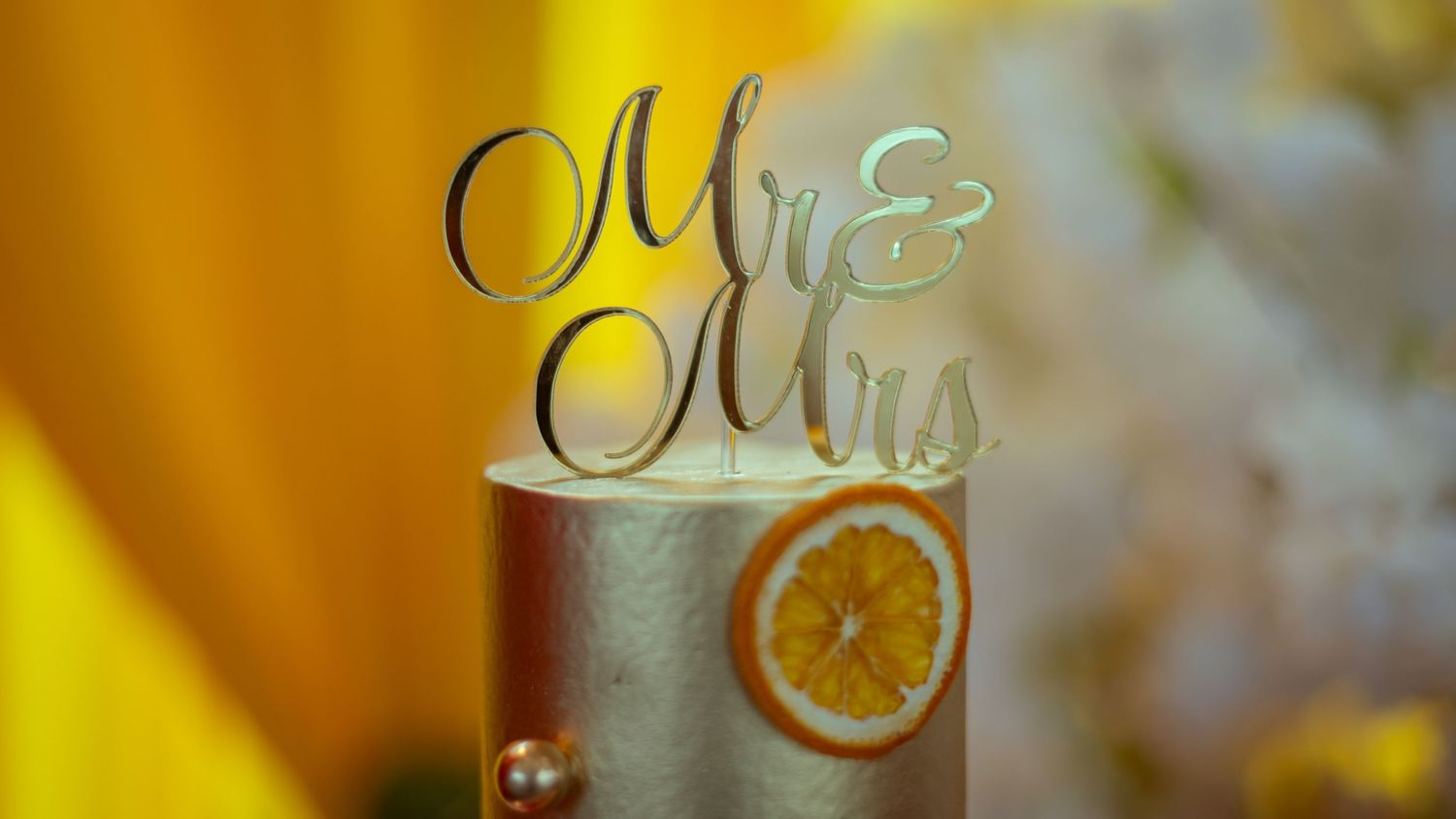 A wedding cake topped with a gold Mr. & Mrs. cake topper, decorated with a dried orange slice.