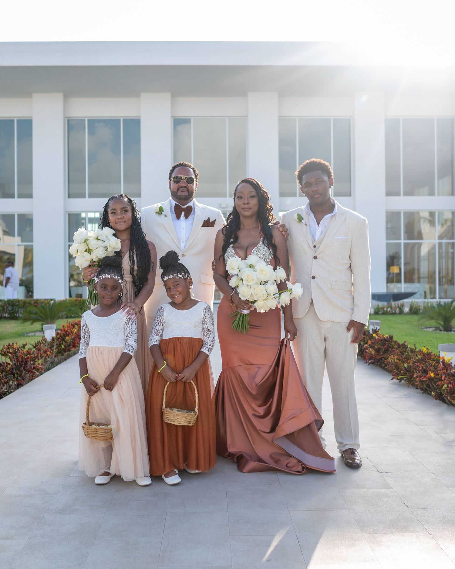 A formal wedding party portrait on a white walkway with a modern building backdrop.