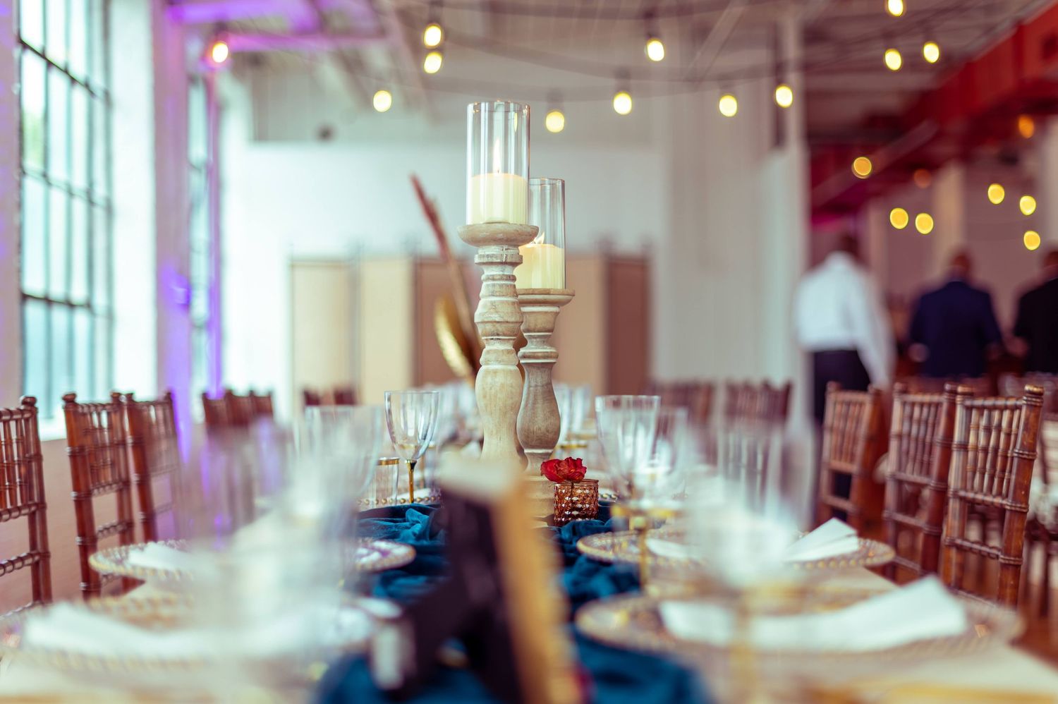 Elegant table setting with tall white candle centerpieces and blue table runners for a formal event.
