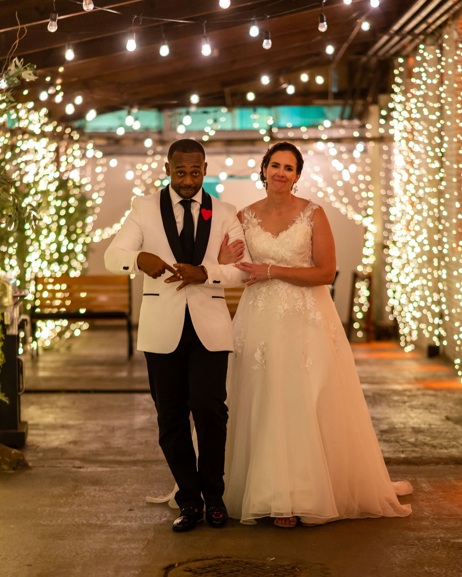 A wedding couple walking under twinkling lights in an indoor venue with romantic ambiance.