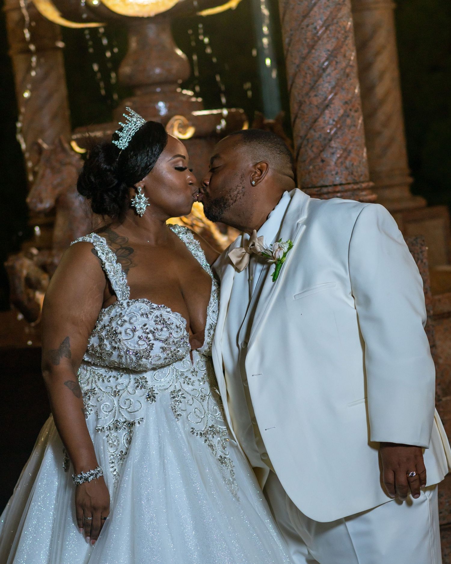 Couple in formal wedding attire sharing intimate moment under ornate lighting.