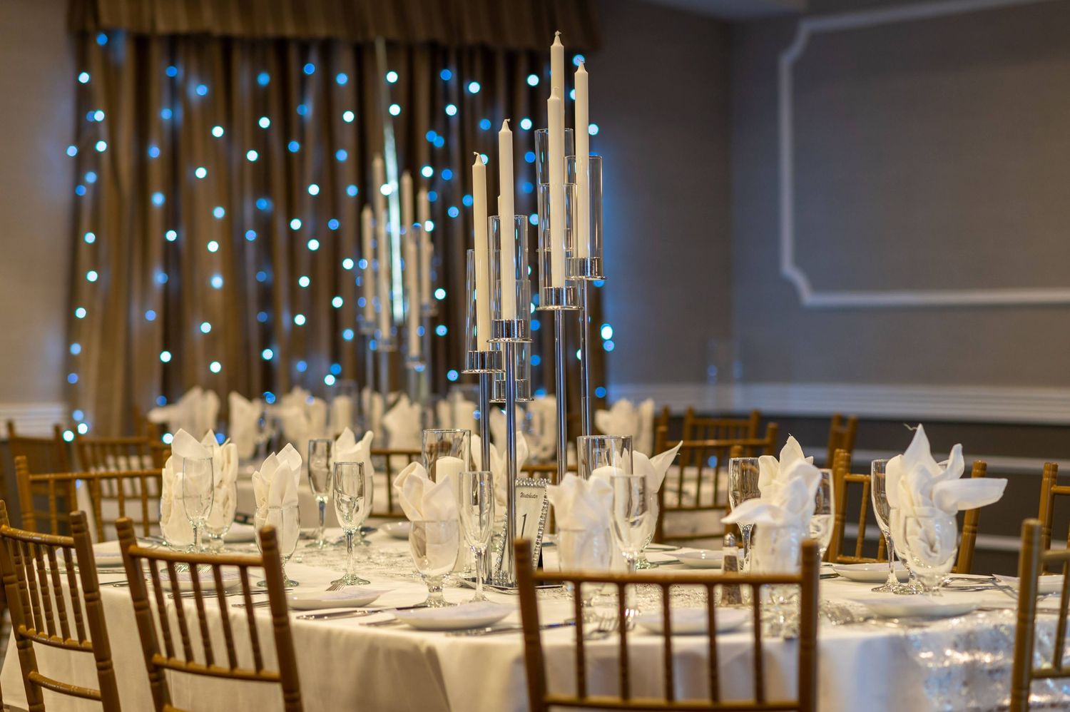 Elegant wedding reception table with tall white candles and place settings.