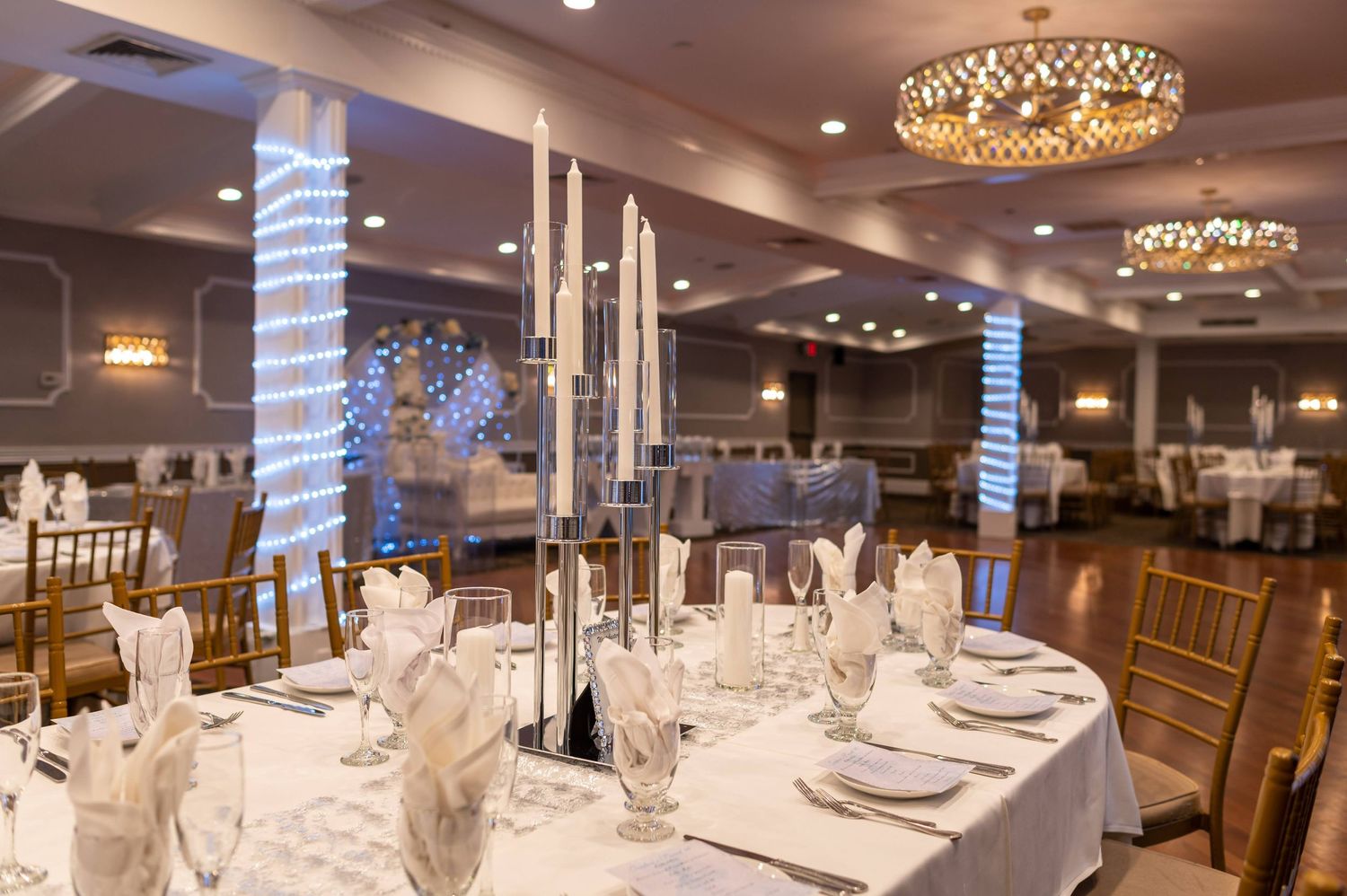 Elegant wedding reception table setting with tall silver candelabras and crystal chandeliers in a banquet hall.