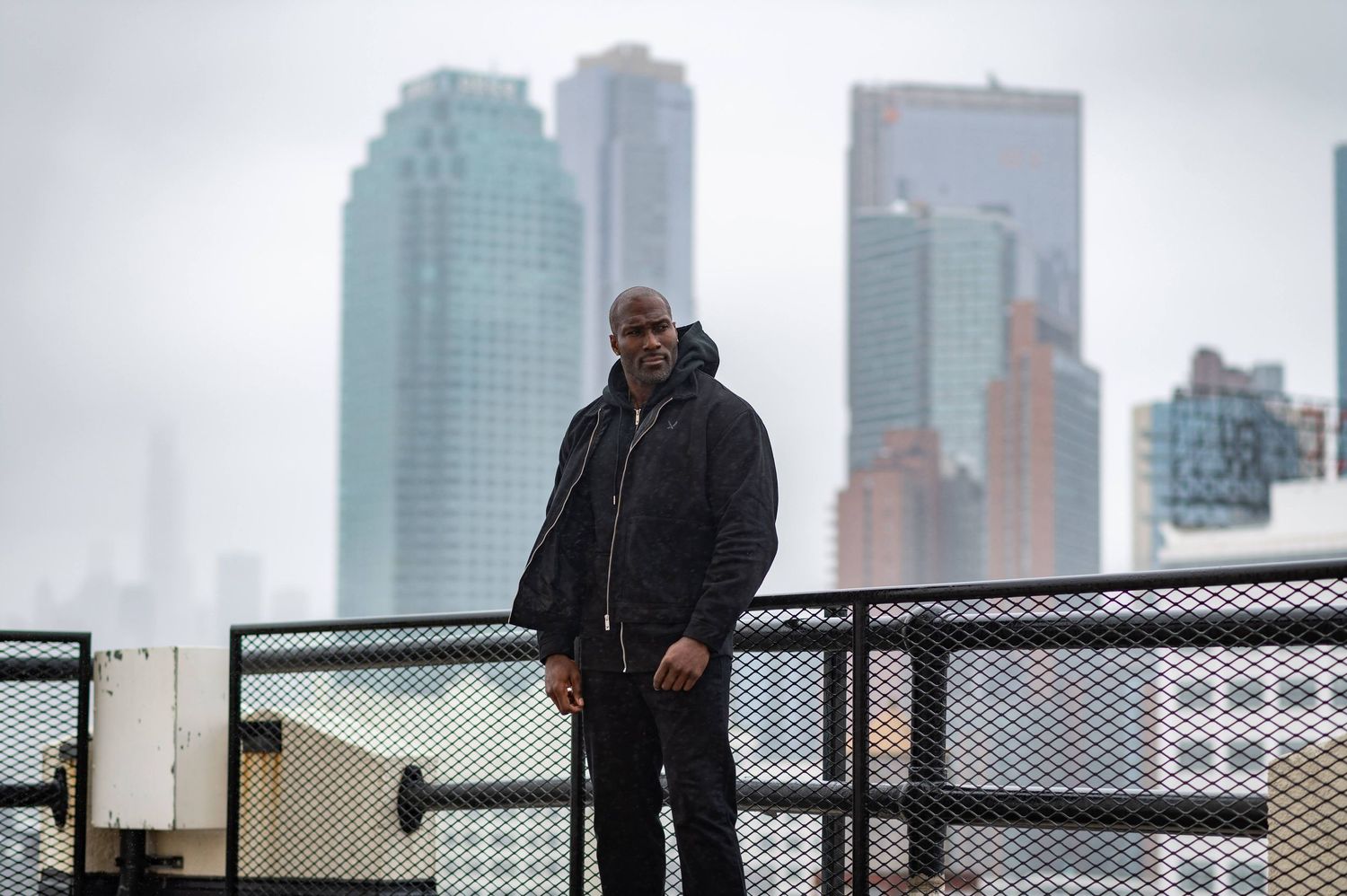 Person in dark winter coat stands against urban skyline with tall buildings in foggy weather.
