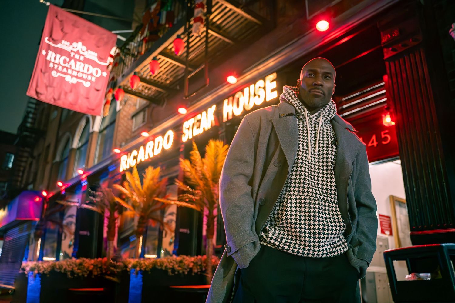 Person stands outside illuminated restaurant with neon signage at night.