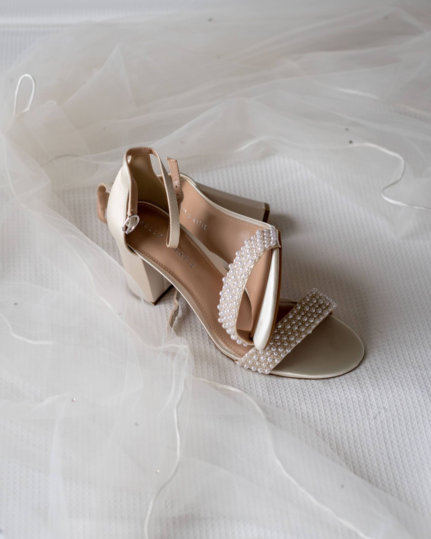 Elegant cream-colored wedding sandals with pearl details on a tulle background.