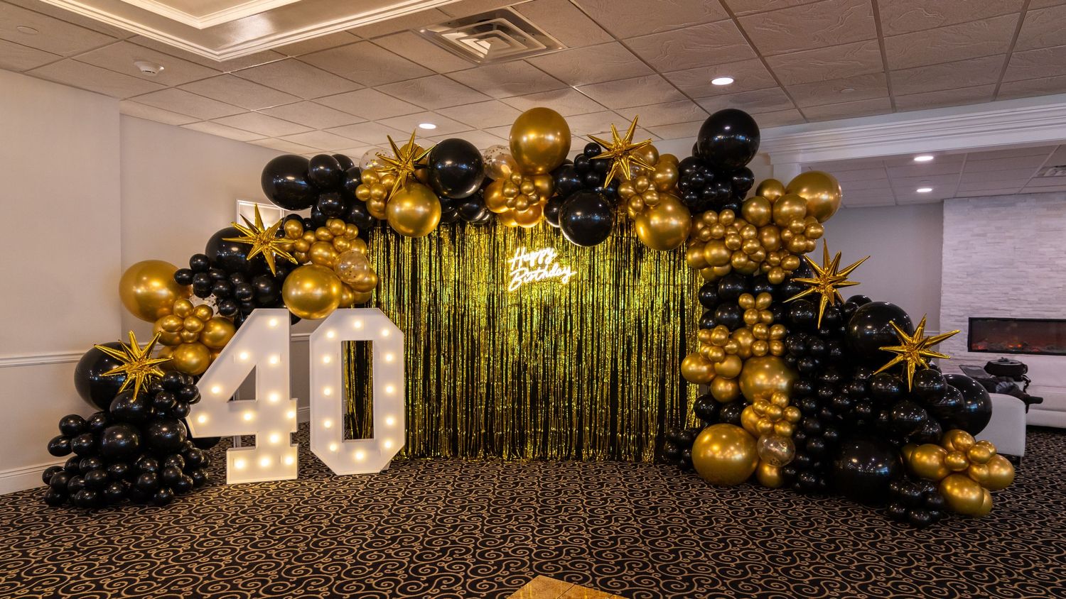 40th birthday celebration display featuring black and gold balloon arch with metallic fringe backdrop.