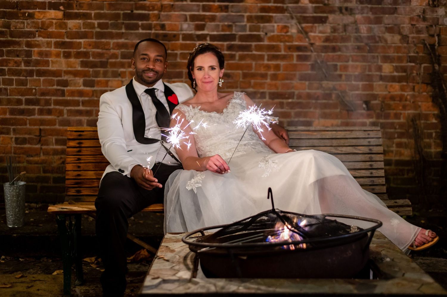 Wedding couple seated by rustic firepit with sparklers creating magical atmosphere.