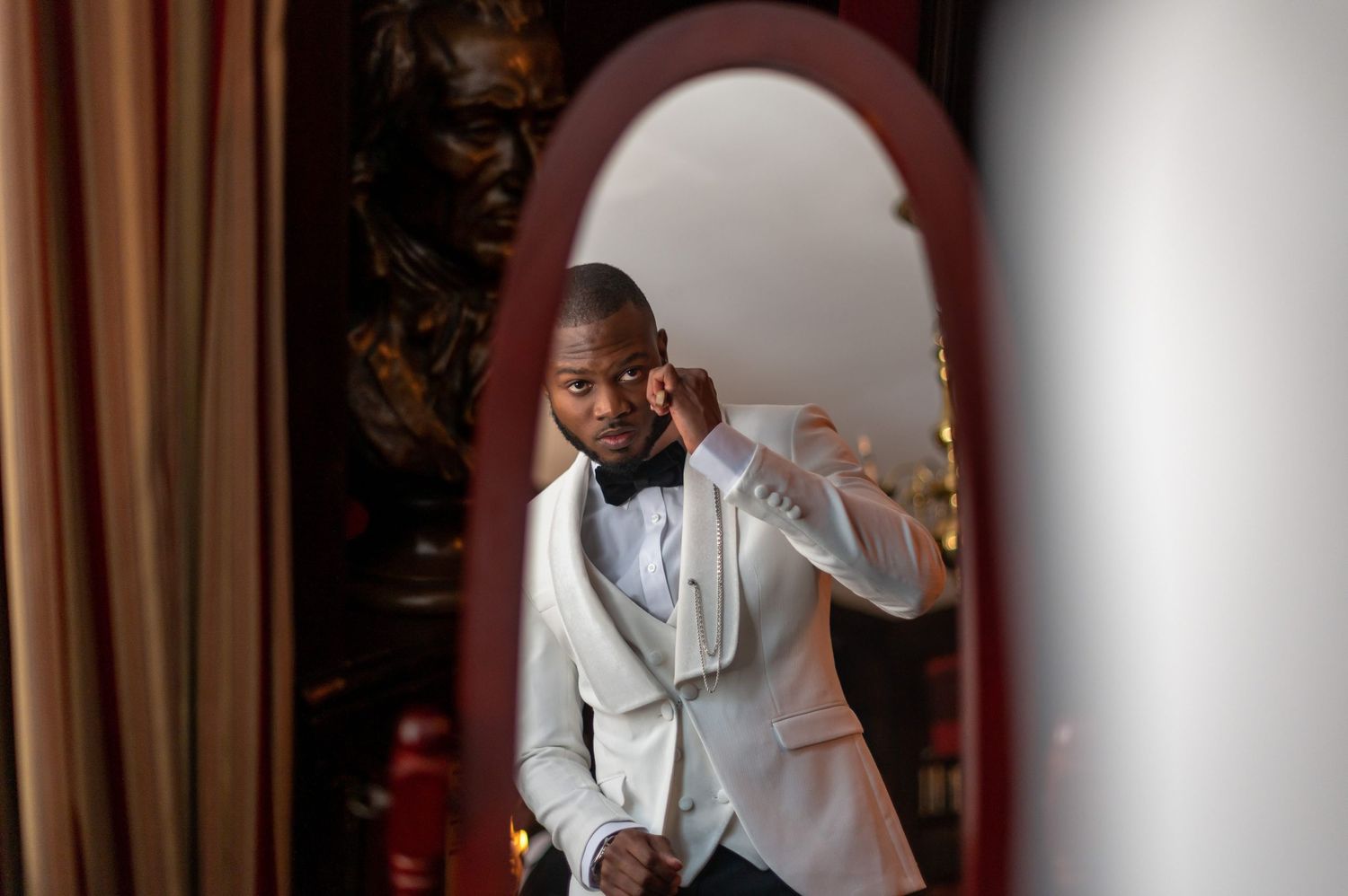 A reflection in a mirror shows a person adjusting their formal white suit jacket.