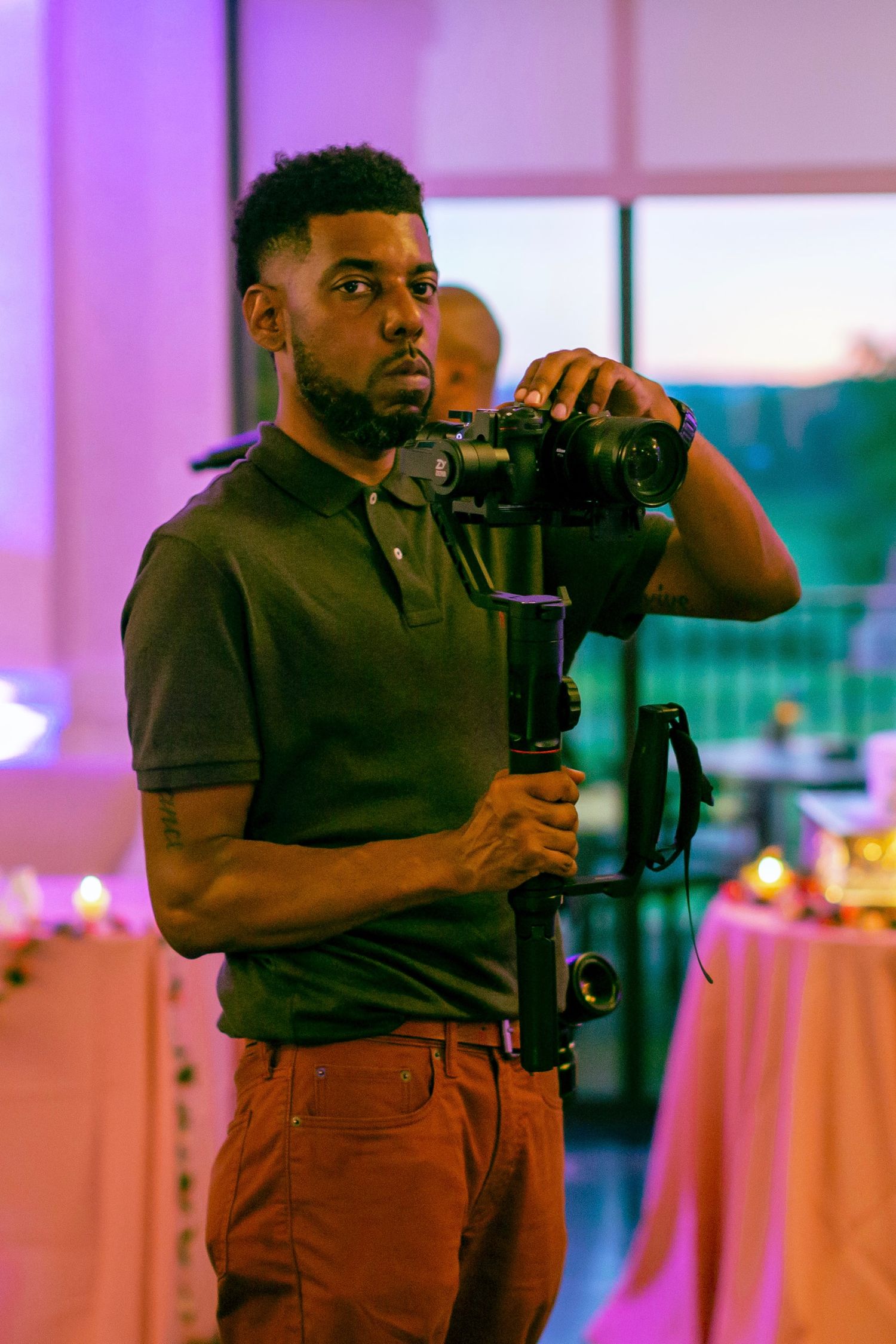 Videographer operating professional camera equipment at an elegant indoor event with pink ambient lighting.