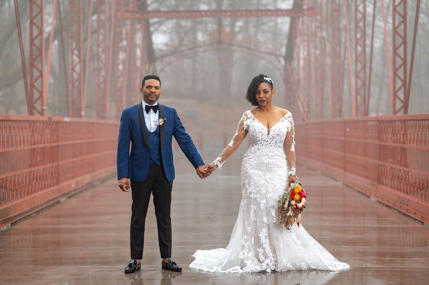 Newlyweds holding hands on foggy red bridge in romantic wedding photo.