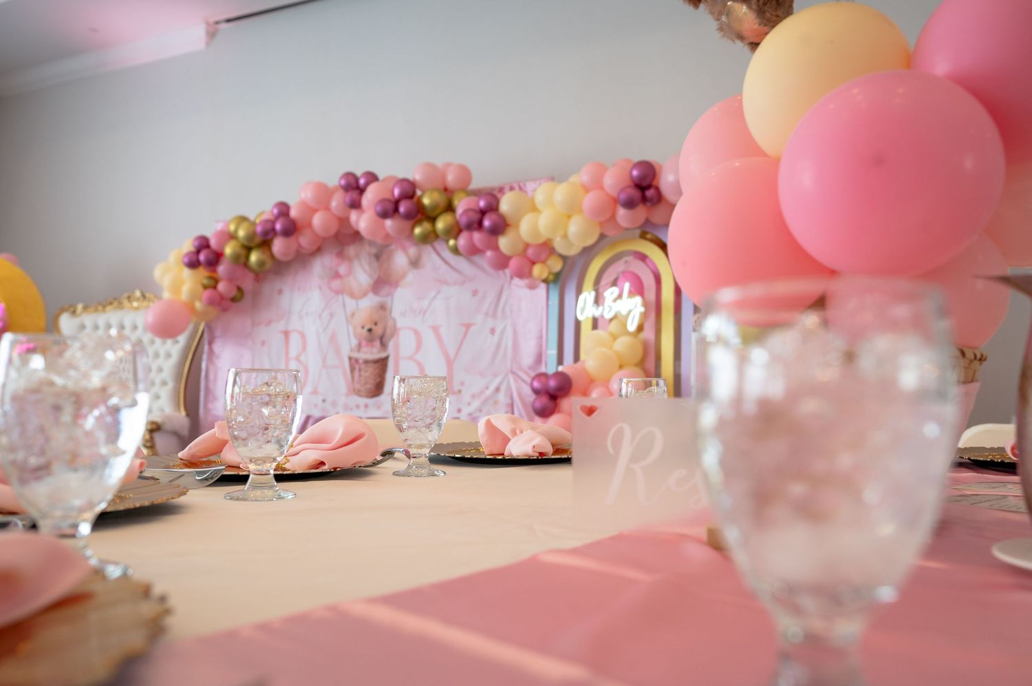 Pink themed party table setting with balloon arch and floral decorations.