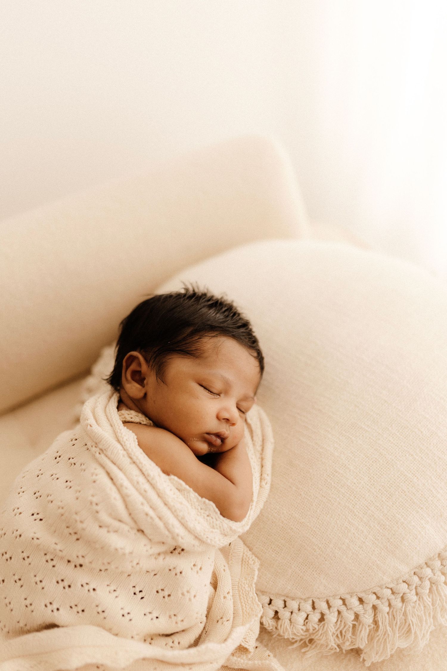 Sleeping newborn wrapped in textured cream blanket on light couch.