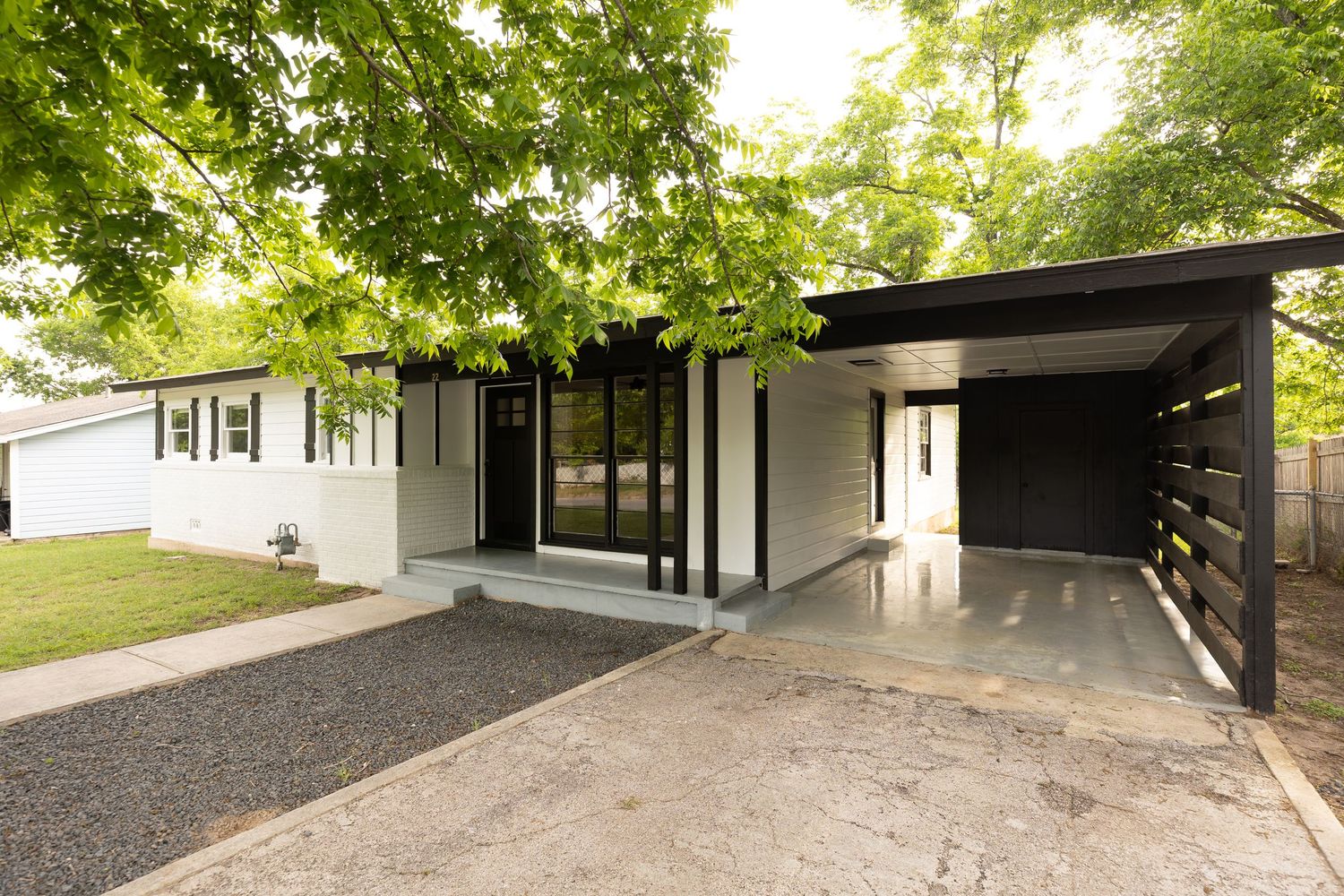Modern ranch home with carport, black trim, and tree-shaded driveway.