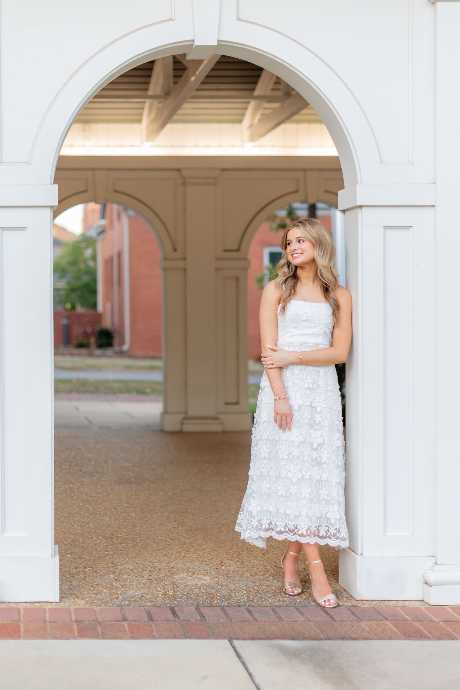 Figure in white lace midi dress poses under architectural archway.