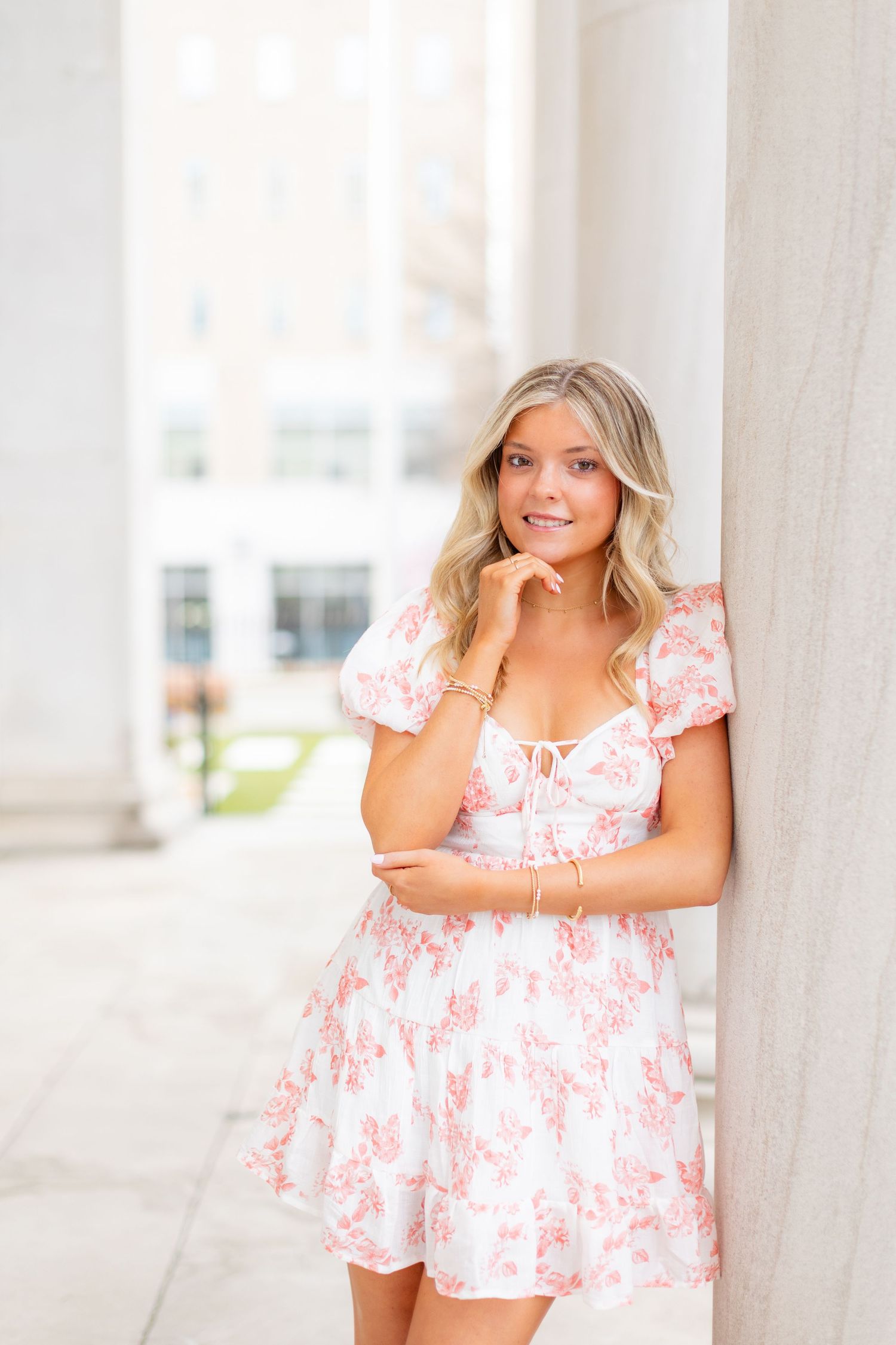 Woman in floral summer dress poses by classical white columns.