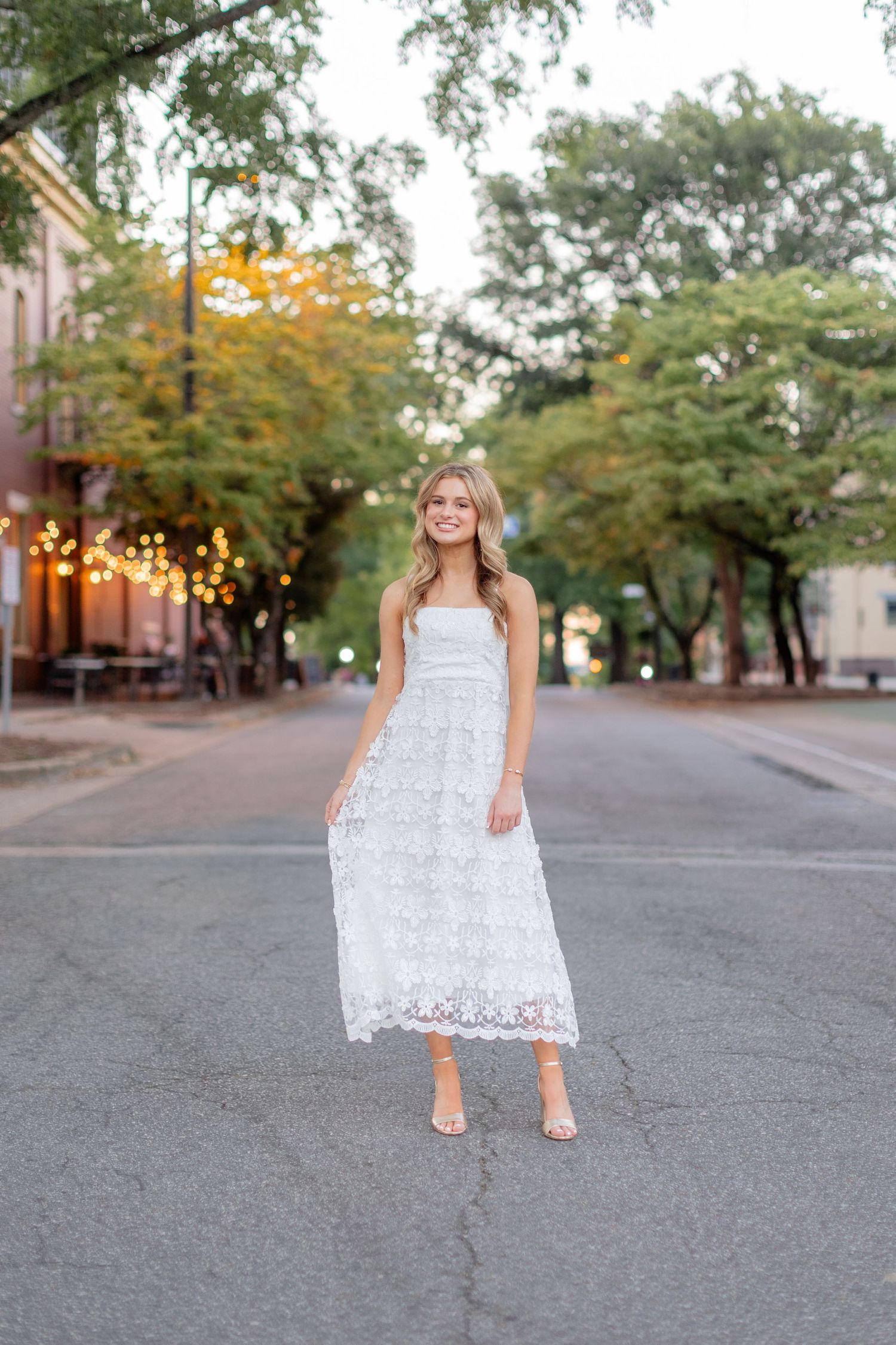 A white lace dress is displayed in a sequence of photos on a street with autumn trees in the background.
