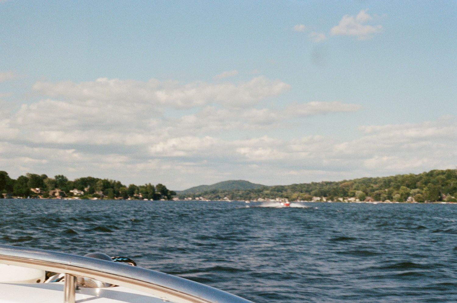 View of a lake dotted with boats and surrounded by tree-lined shores on a sunny day.