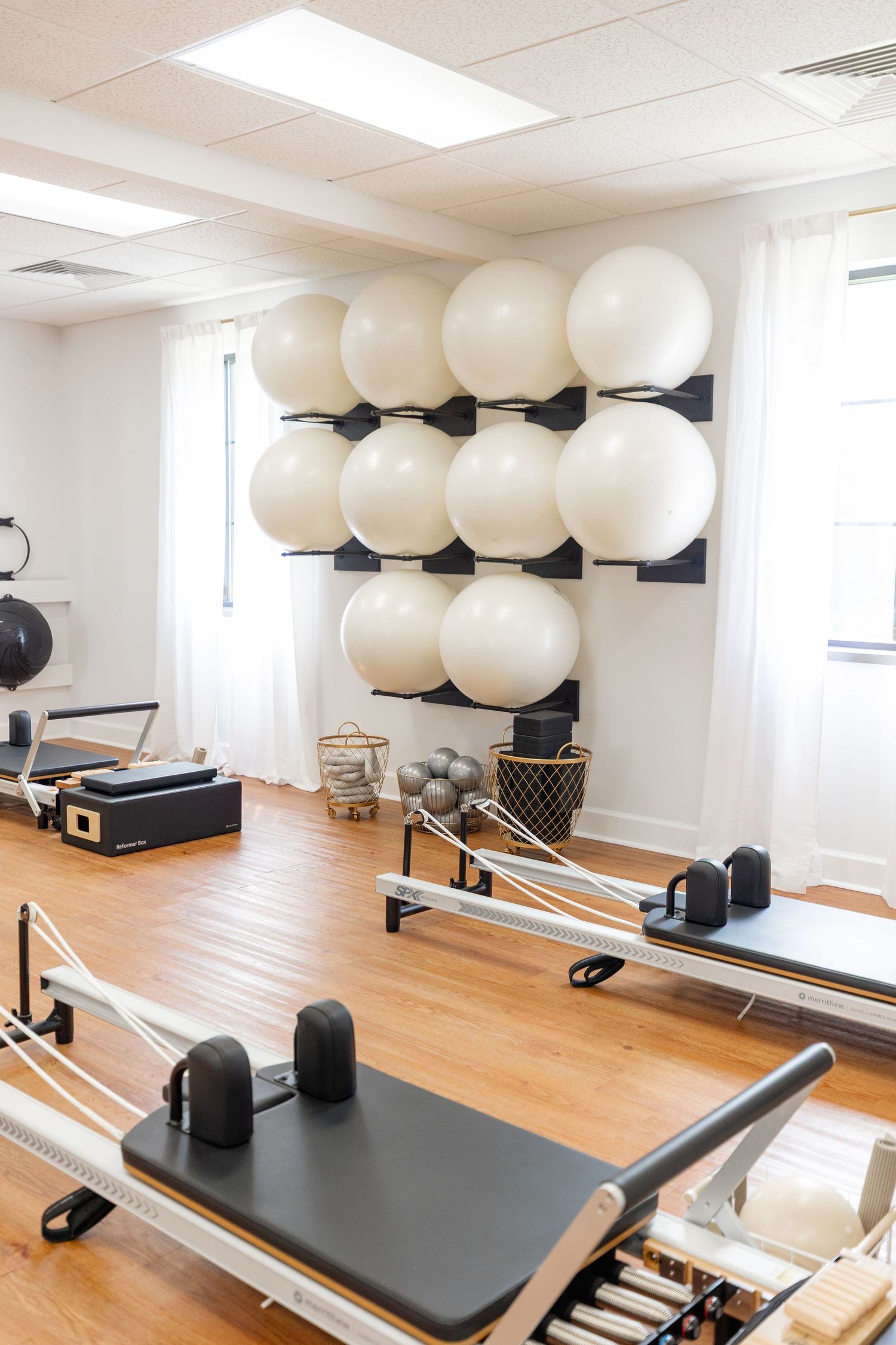 Bright fitness studio with pilates reformers and stability balls mounted on wall.