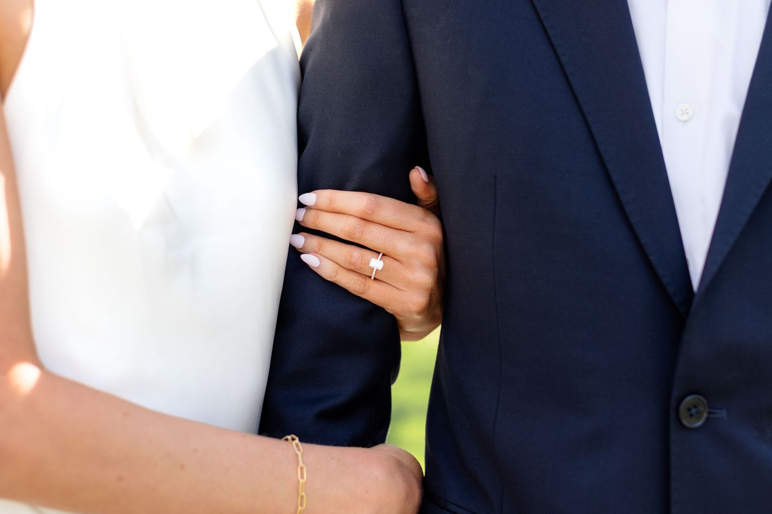 A row of wedding guests in formal attire stand together outdoors for a group photo.
