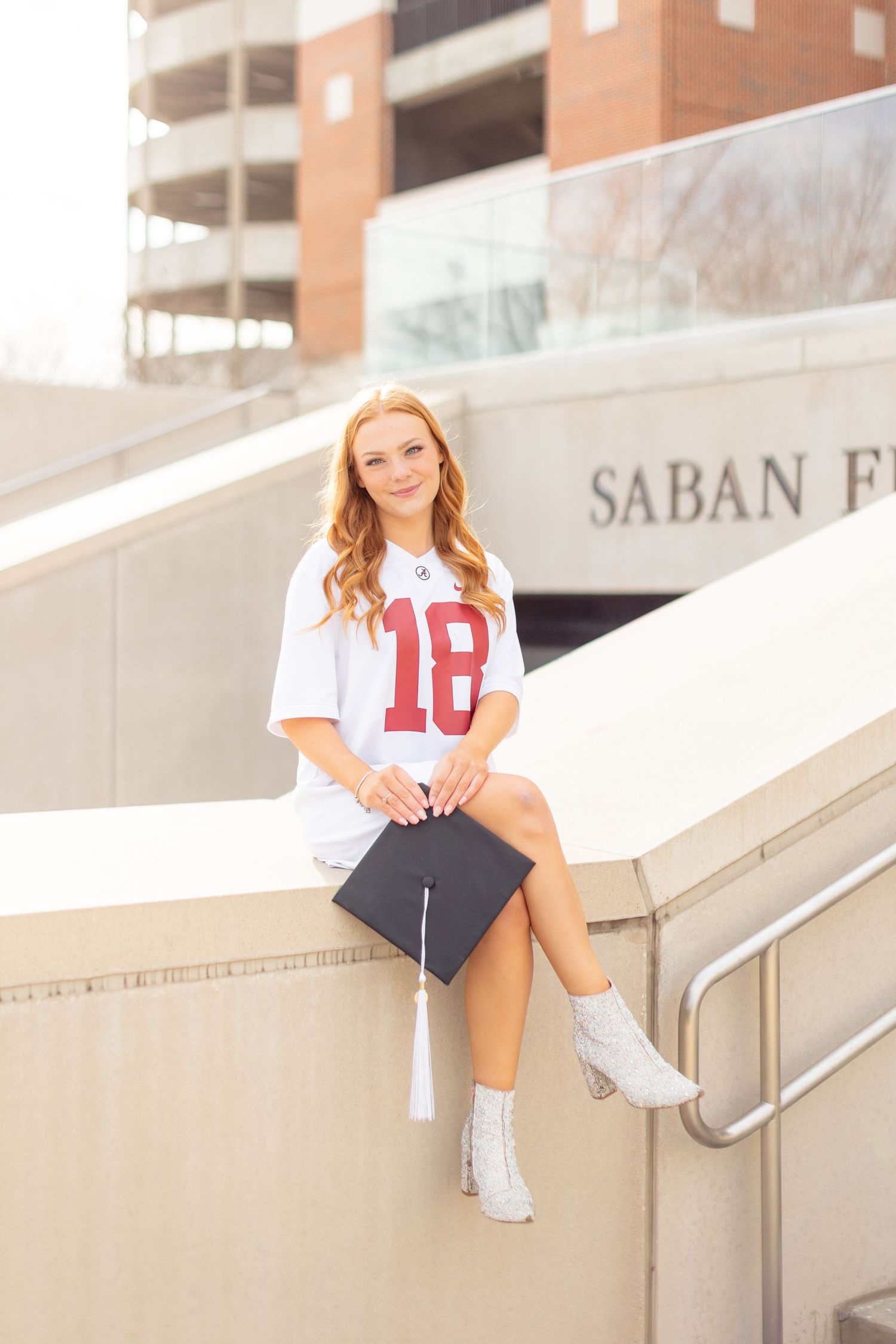 Young athlete in white jersey number 10 sitting on concrete stadium steps in bright sunlight.