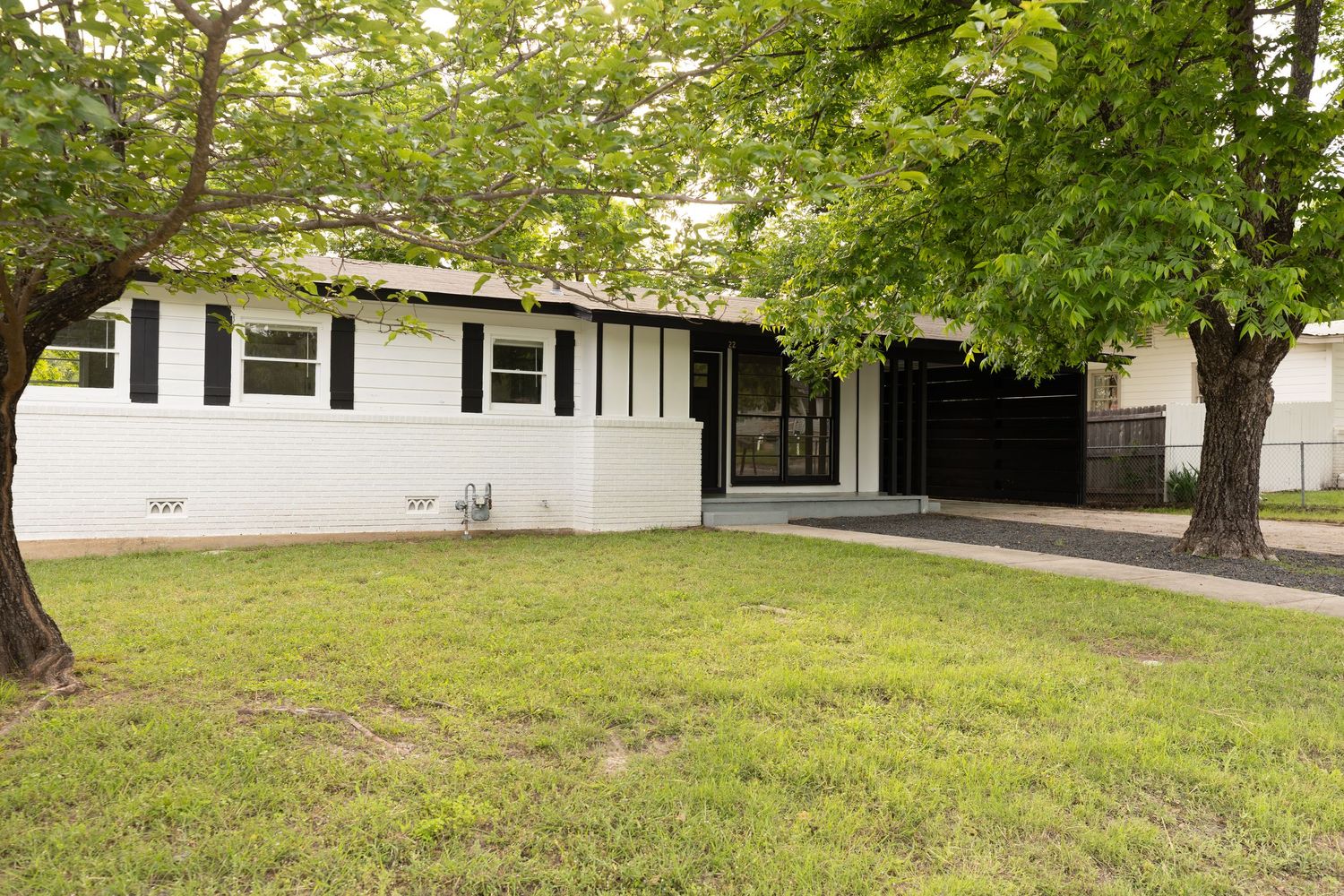 White ranch-style home with black shutters, large shade trees, and well-maintained green lawn.