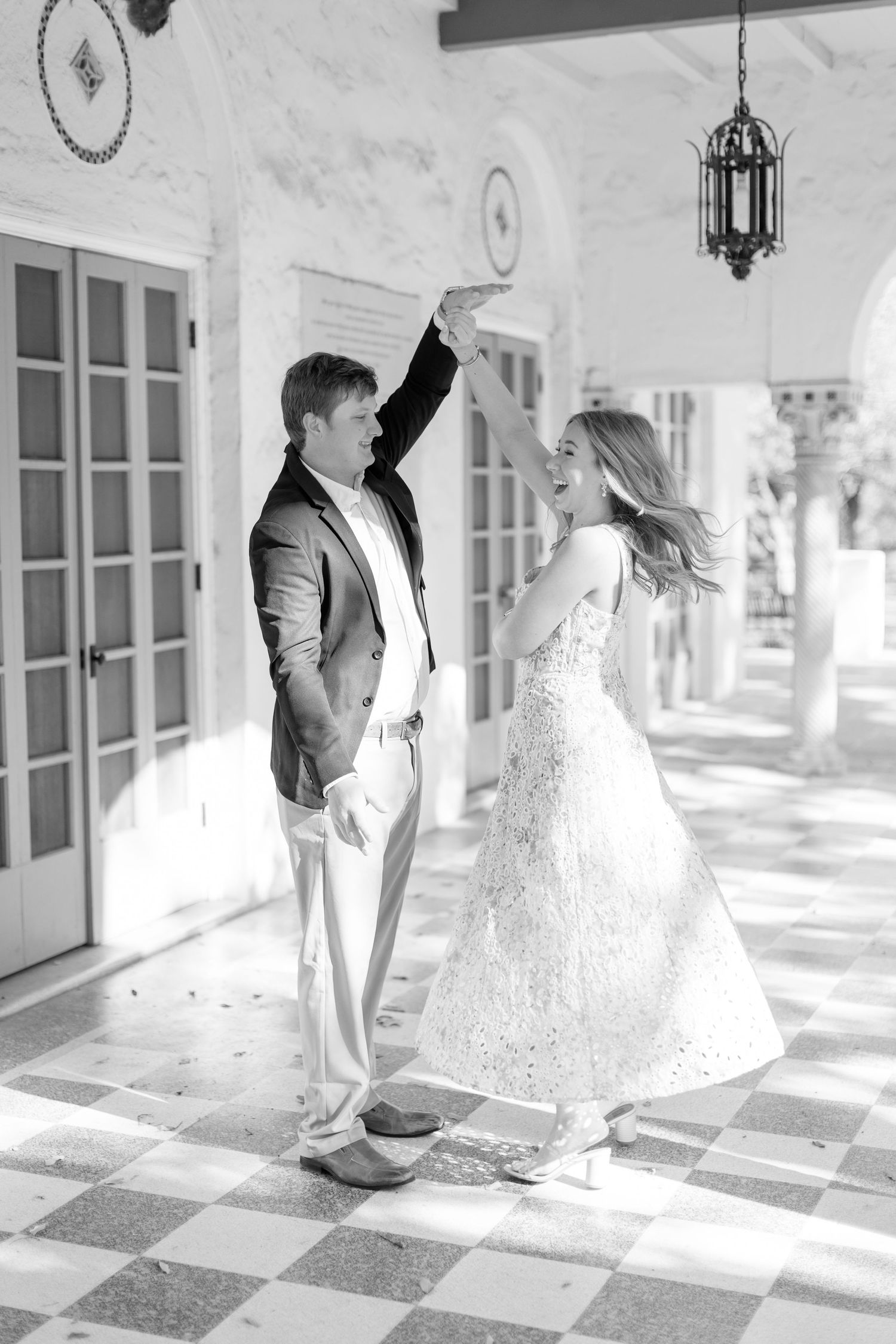 Black and white wedding photos showing couple walking on checkered floor in elegant venue with sunlit windows and arches.