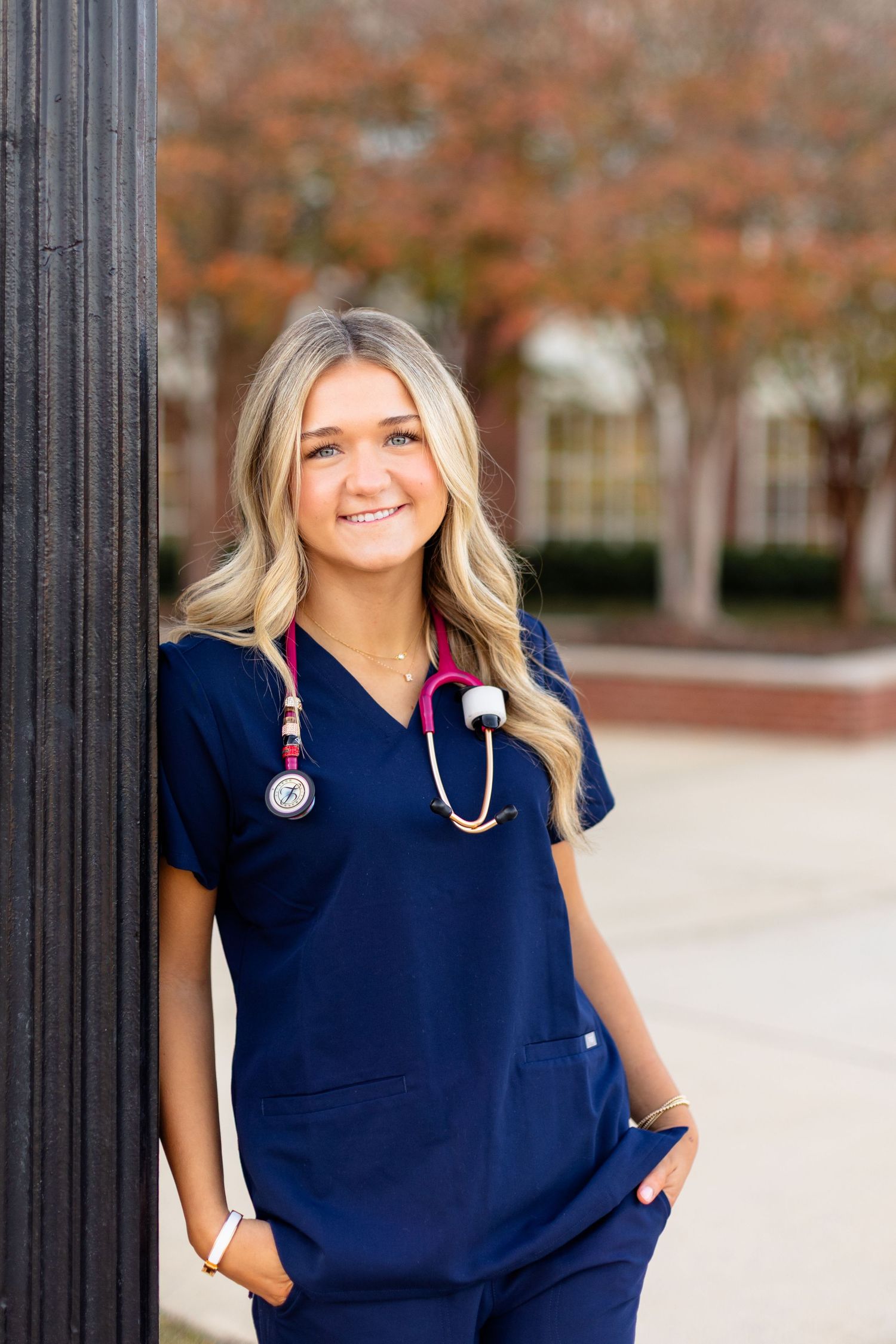 Healthcare professional in navy blue scrubs and stethoscope smiling in outdoor medical setting.