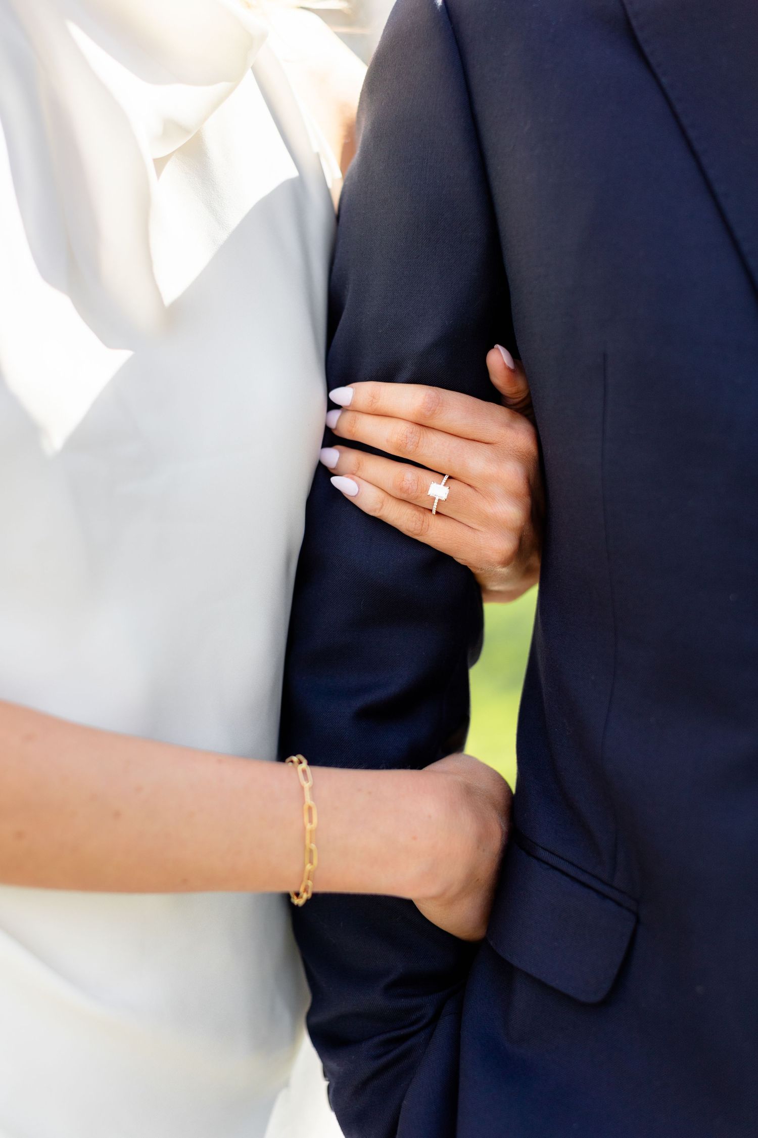 Close-up view of wedding couple's arms embracing, showing formal attire with navy suit and white dress details.