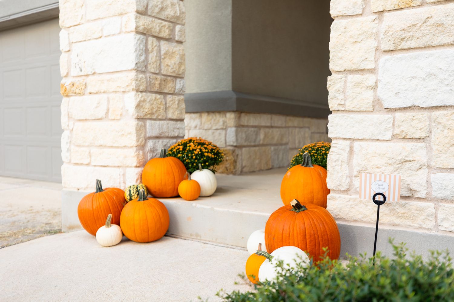 Orange pumpkins and fall decorations arranged on a stone porch with white columns create a festive autumn display.