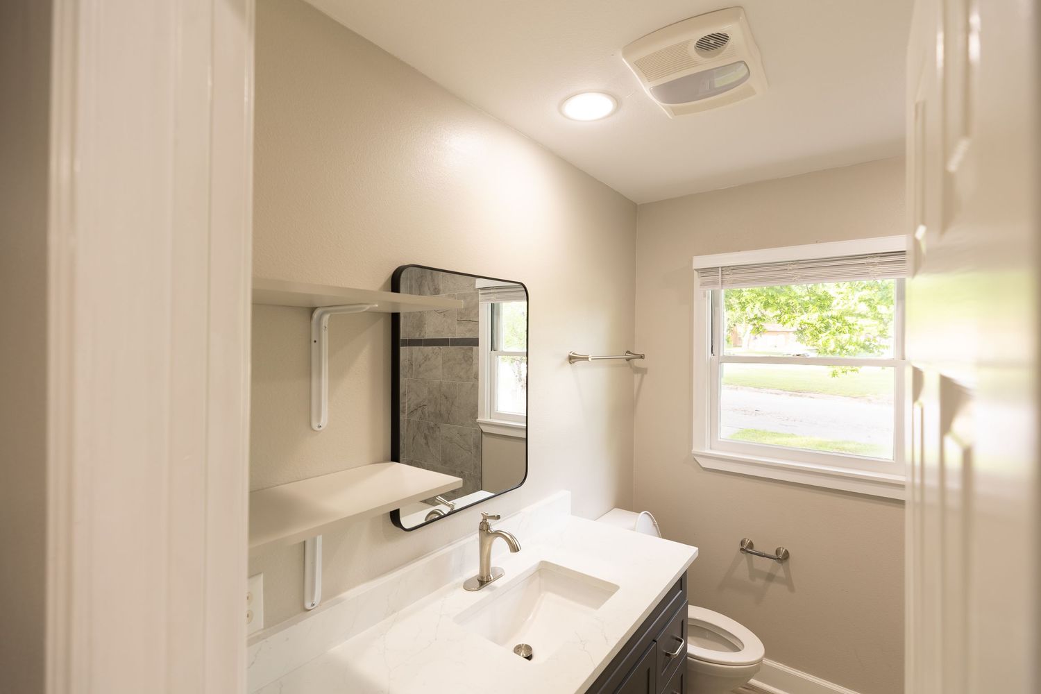 Modern bathroom with white vanity, square sink, framed mirror, and bright window in a neutral-toned space.