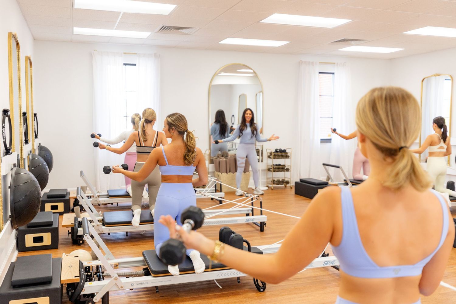 Women exercising on pilates reformer machines in bright studio with mirrors.