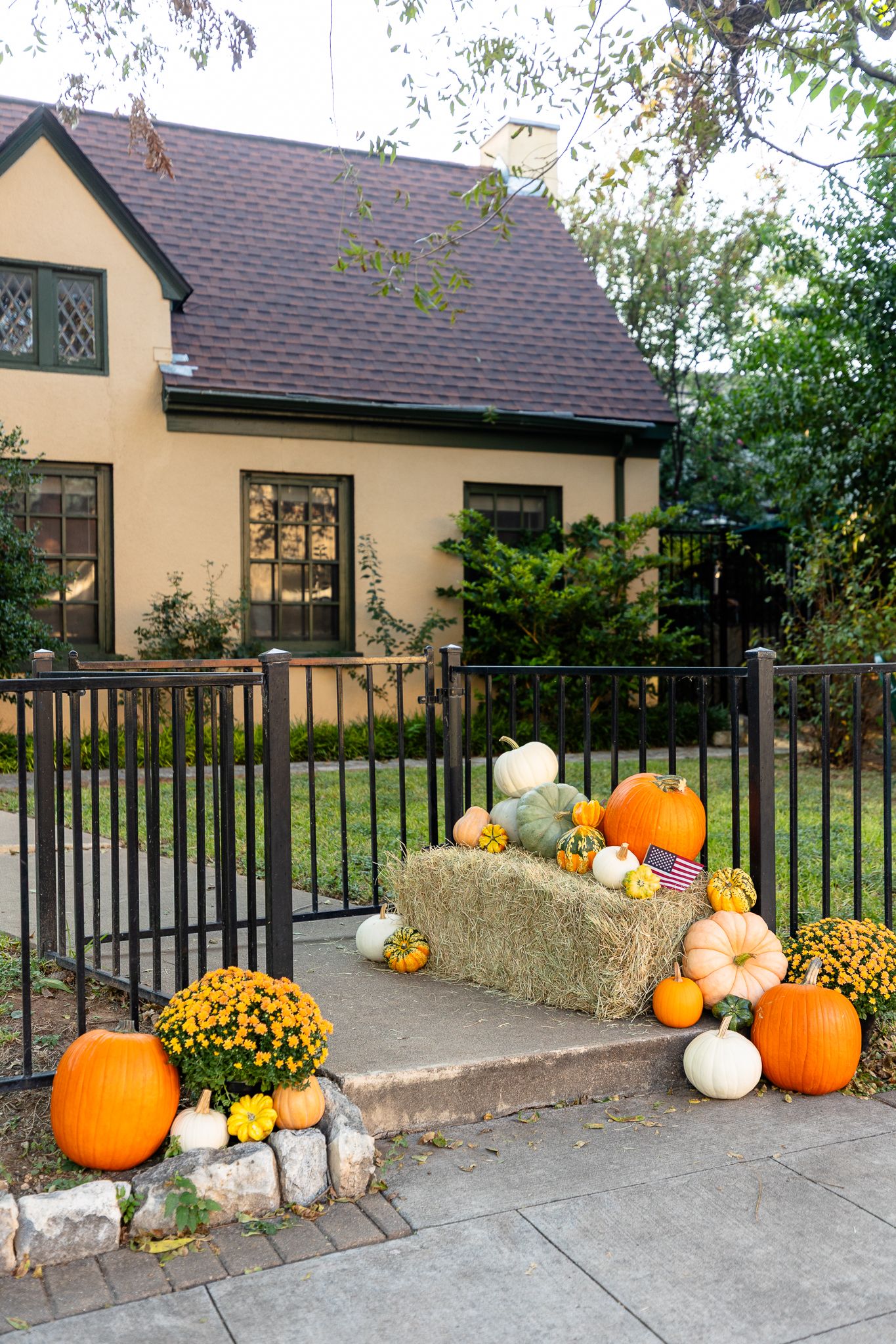 Panoramic view of a house entrance decorated with autumn pumpkins, hay bales, and orange mums for fall season.
