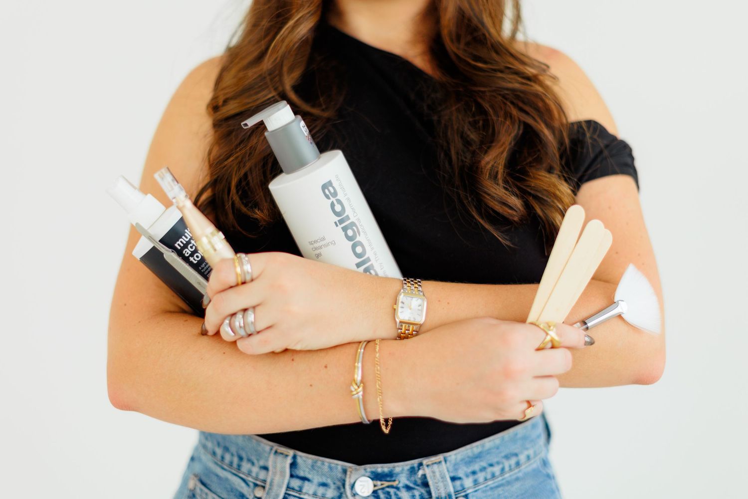 Woman holding hair styling tools and Edique hair care products, wearing gold bracelets and rings.
