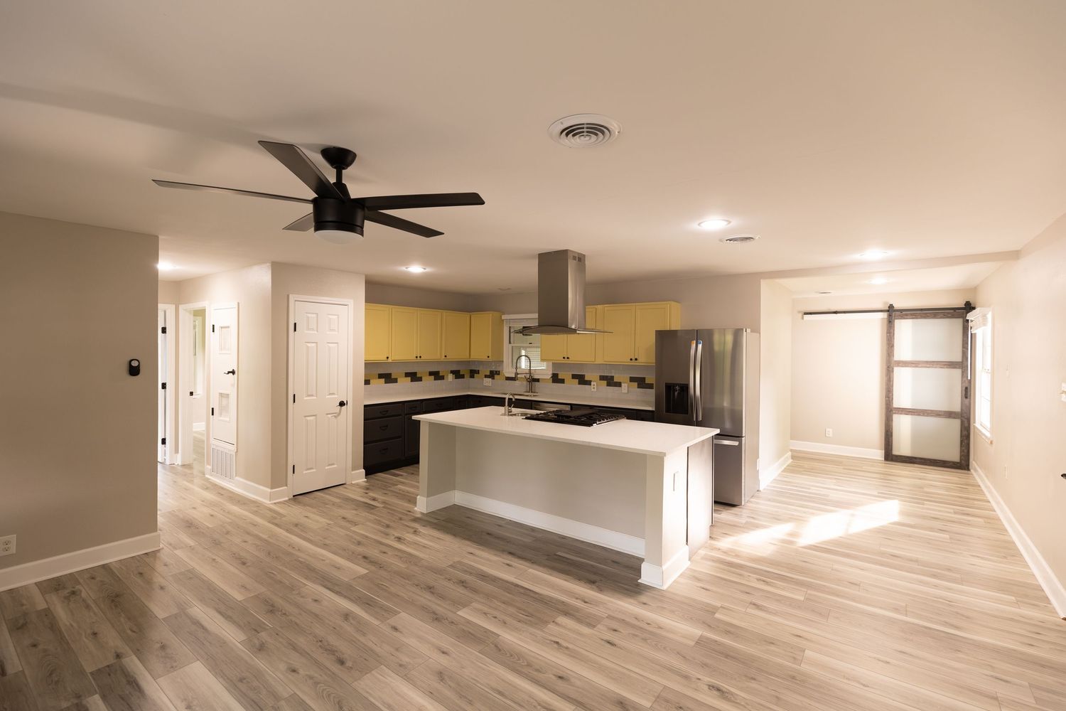 Modern open-concept kitchen with yellow cabinets, island, stainless steel appliances, and light hardwood floors.