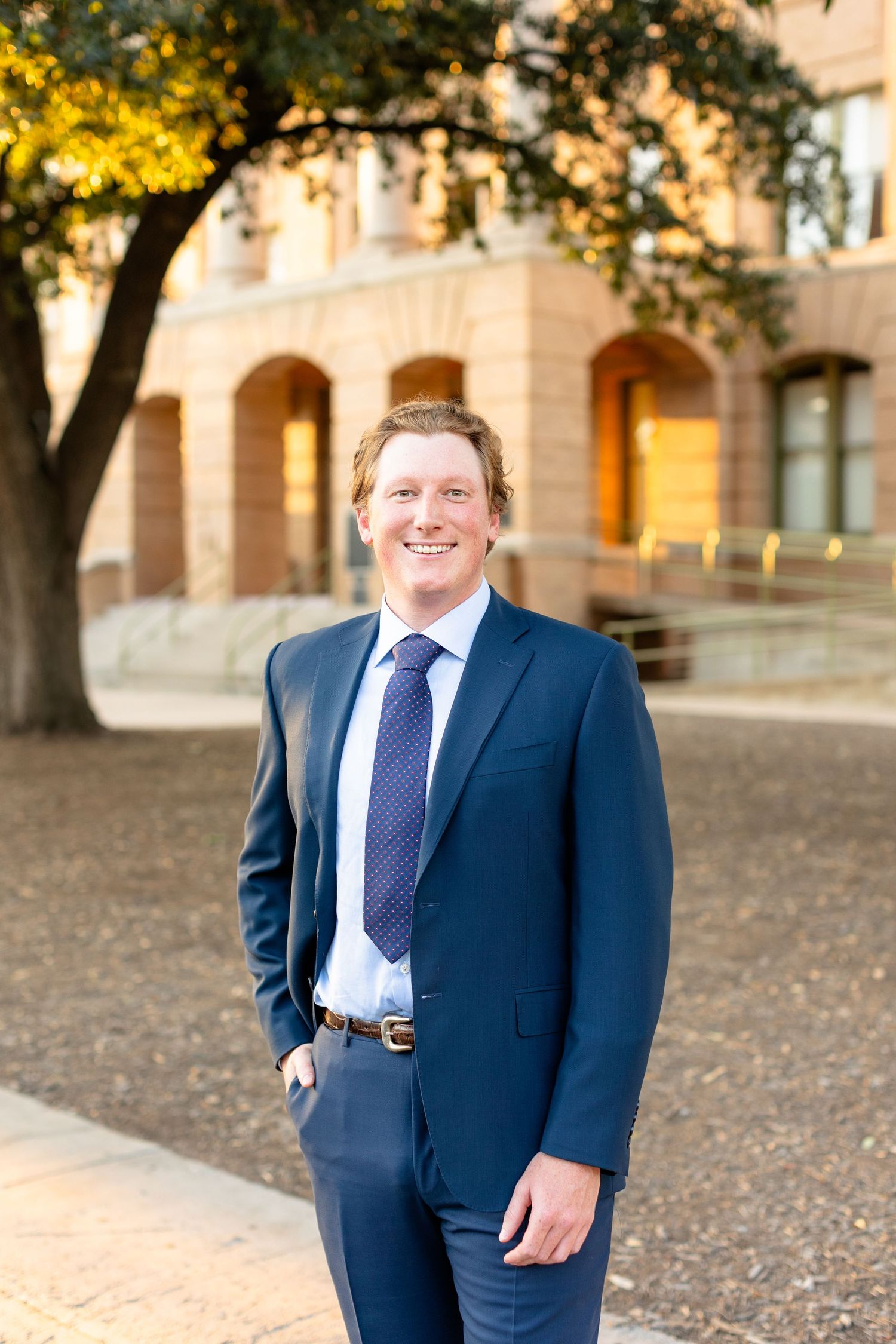 Professional portrait session on a college campus with autumn leaves and arched architecture in the background.