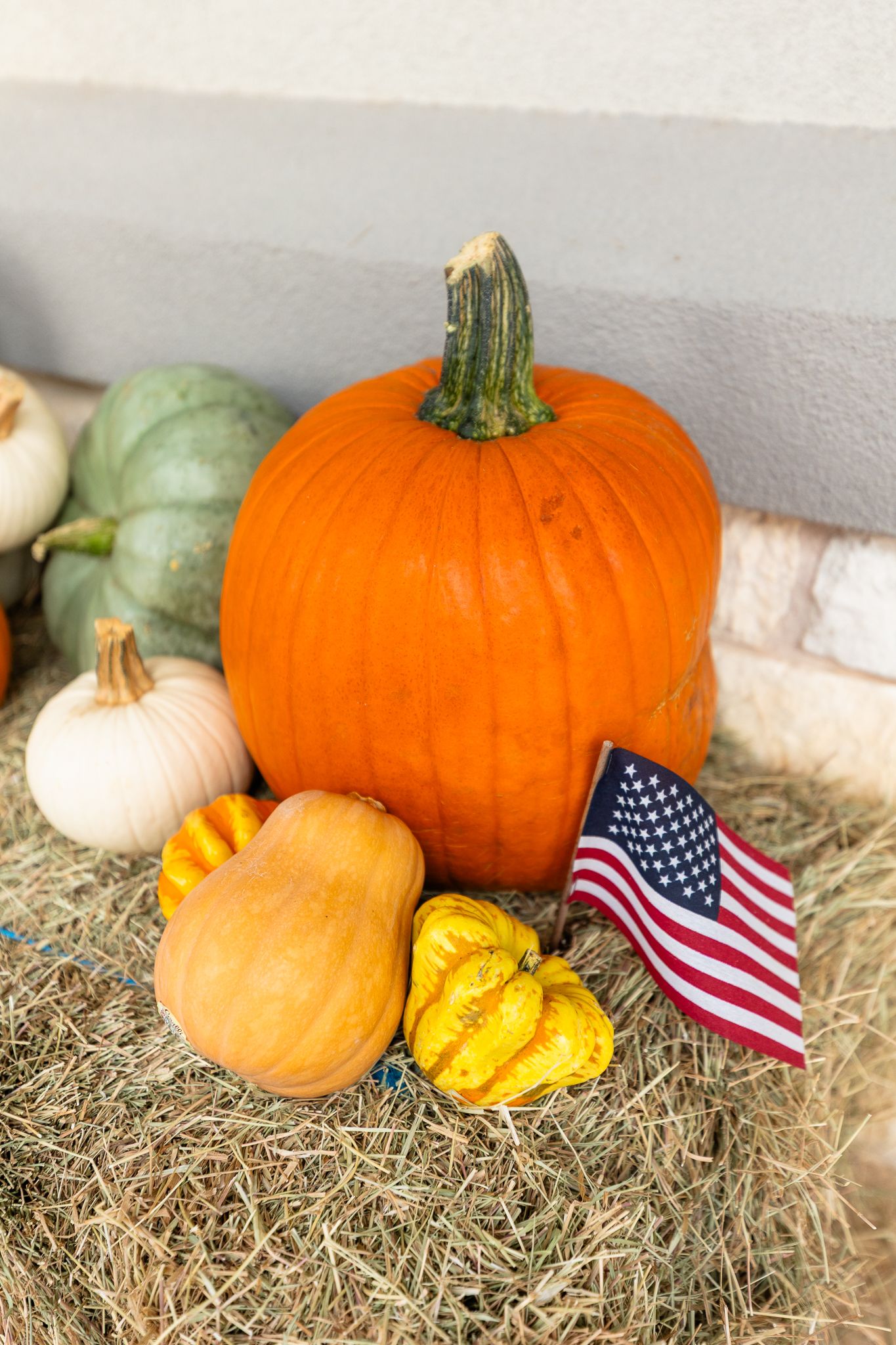 Festive autumn display showing orange and white pumpkins arranged on hay bales with small American flags.