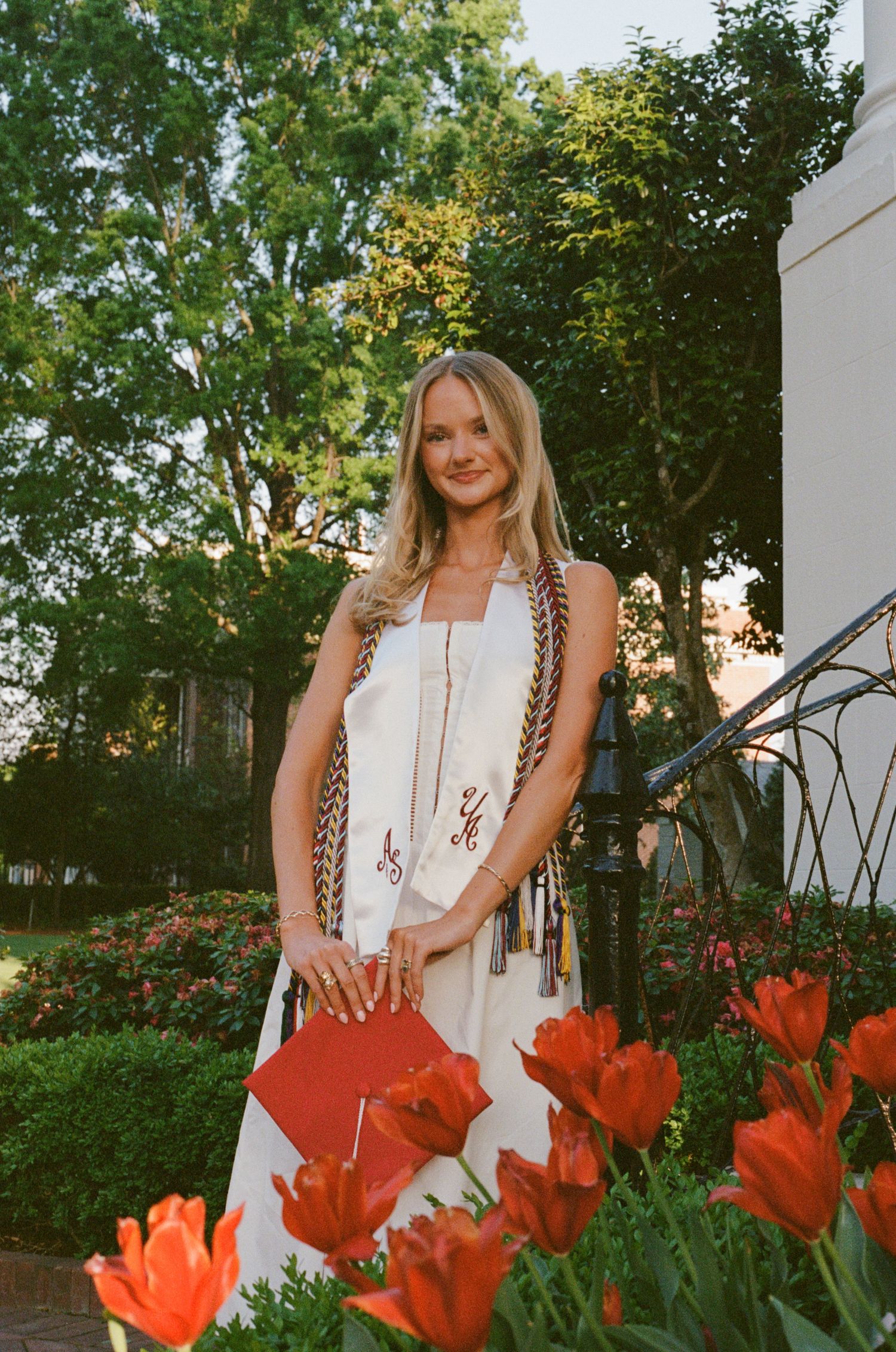 Woman in white dress poses in garden with vibrant red tulips in foreground during golden hour.