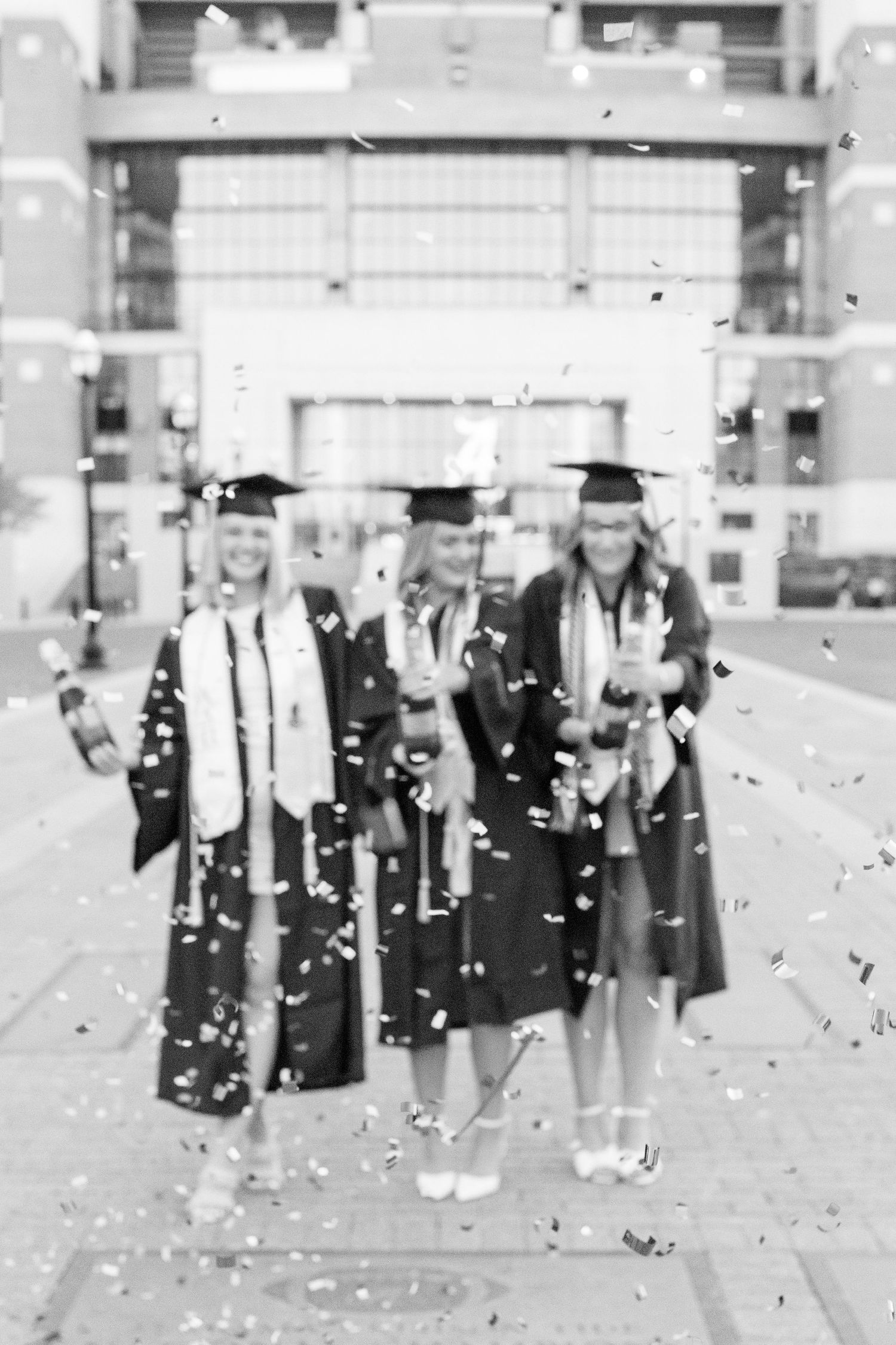 Black and white photo of graduates celebrating with confetti in front of stadium.