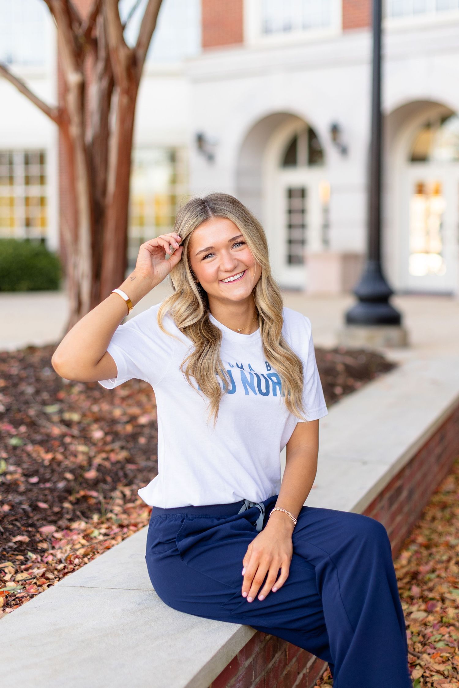 Student wearing a navy and white university outfit sits casually on a concrete ledge outside a campus building.