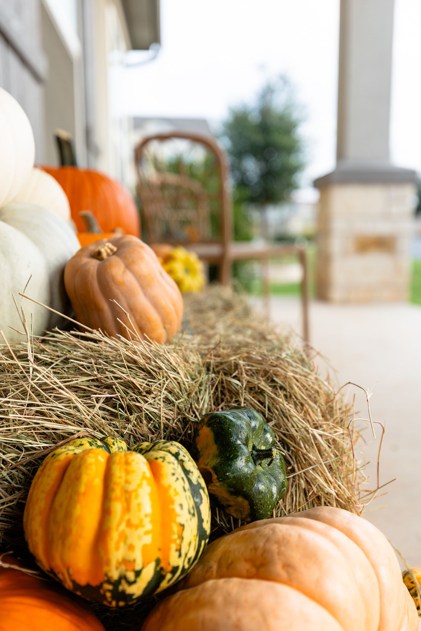 Decorative autumn pumpkins and gourds arranged on hay bales create a festive fall display on a covered porch.