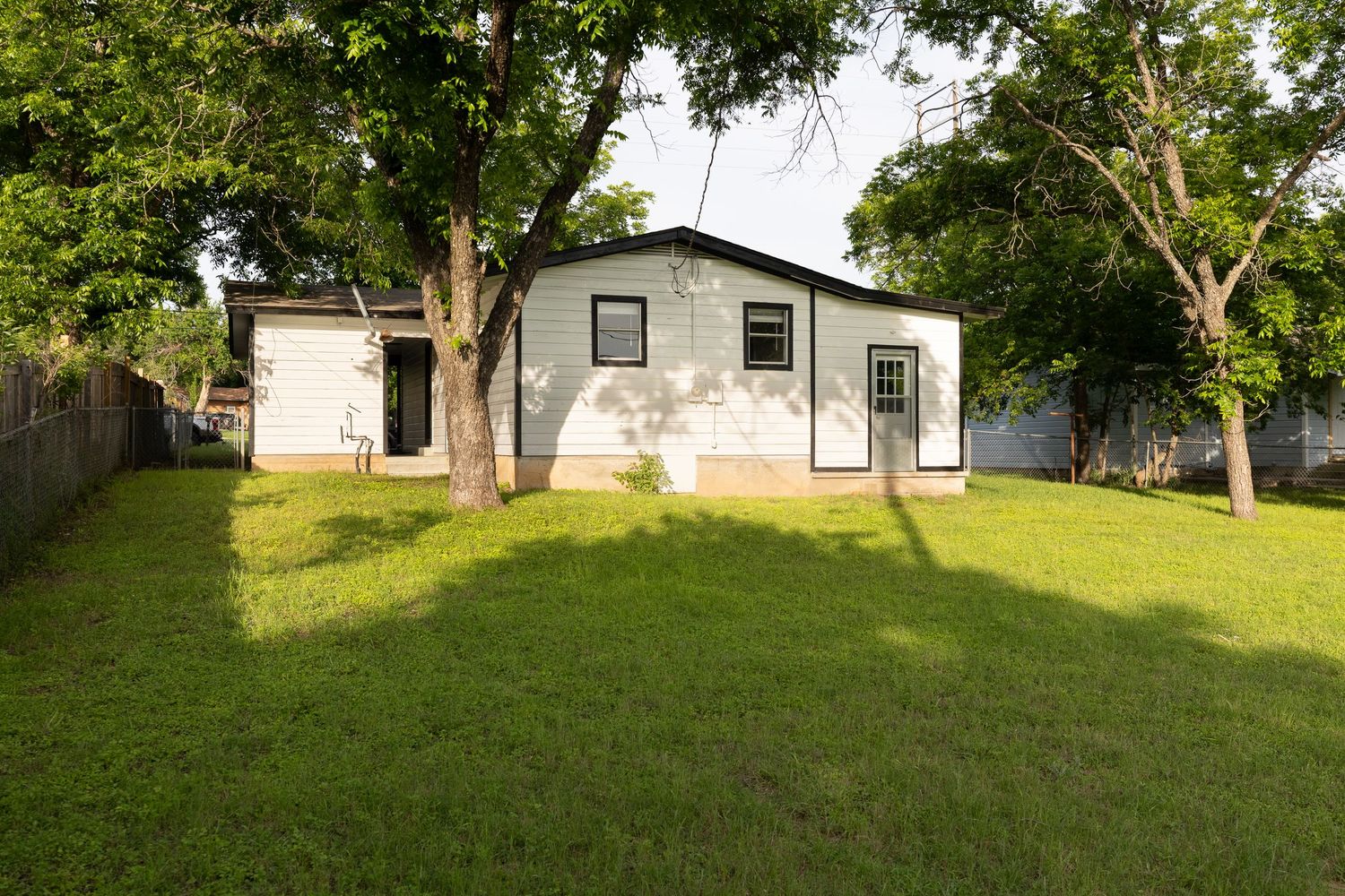 Exterior view of white ranch home surrounded by lush green grass and trees.