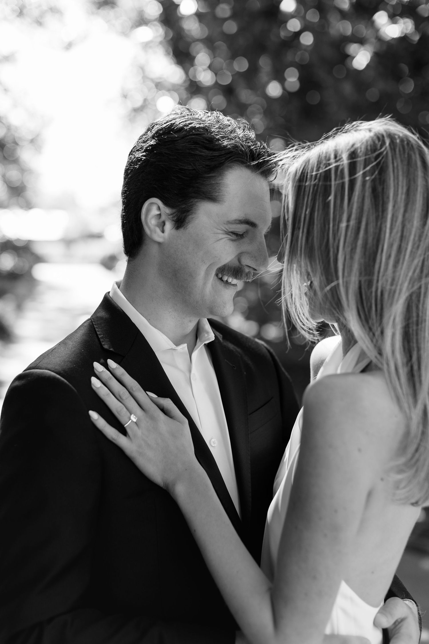 A joyful black and white engagement photo showing a couple sharing an intimate moment outdoors with bokeh lighting.